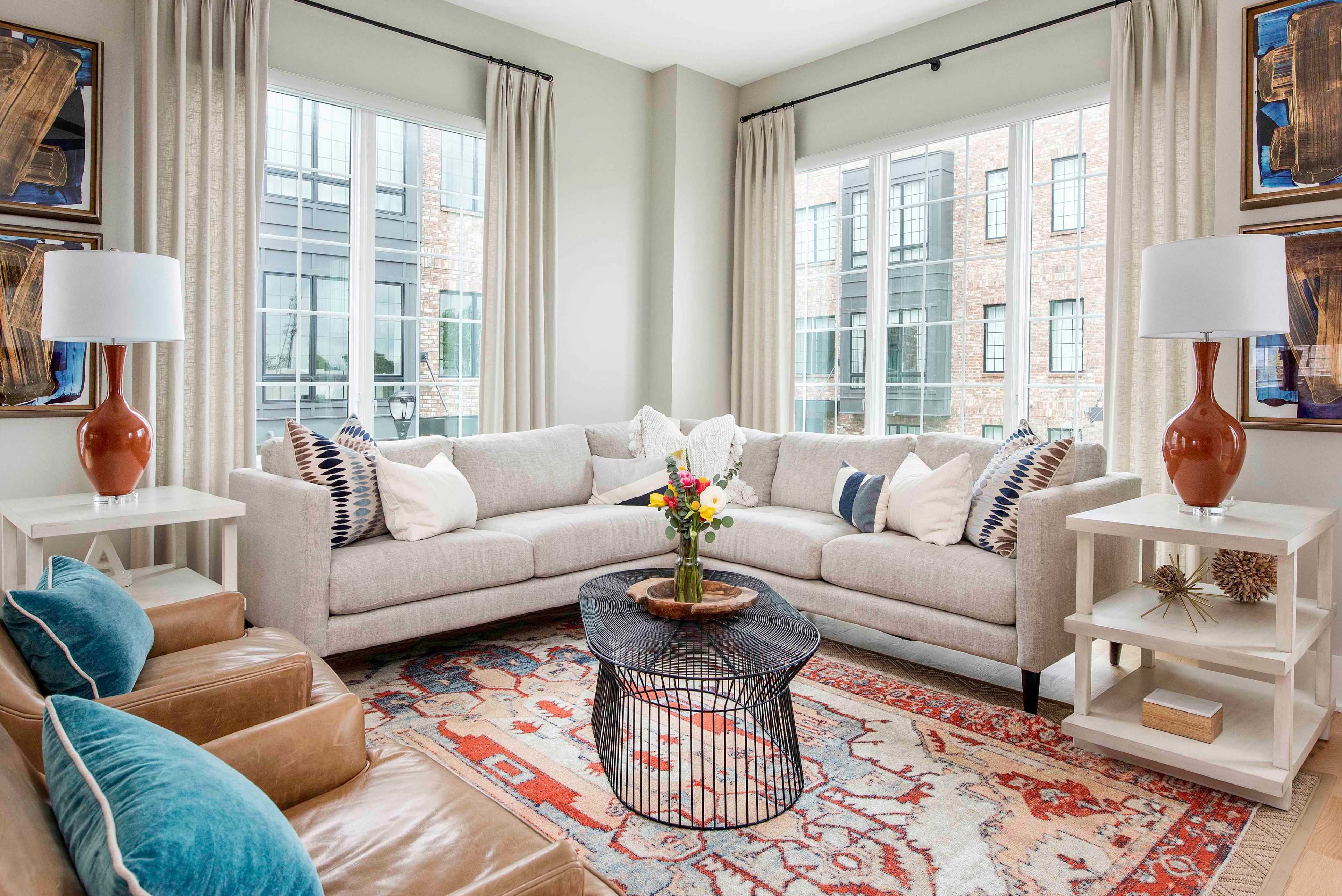 A modern living room with a light gray sectional sofa, decorative pillows, a wooden coffee table, and large windows overlooking an urban setting.