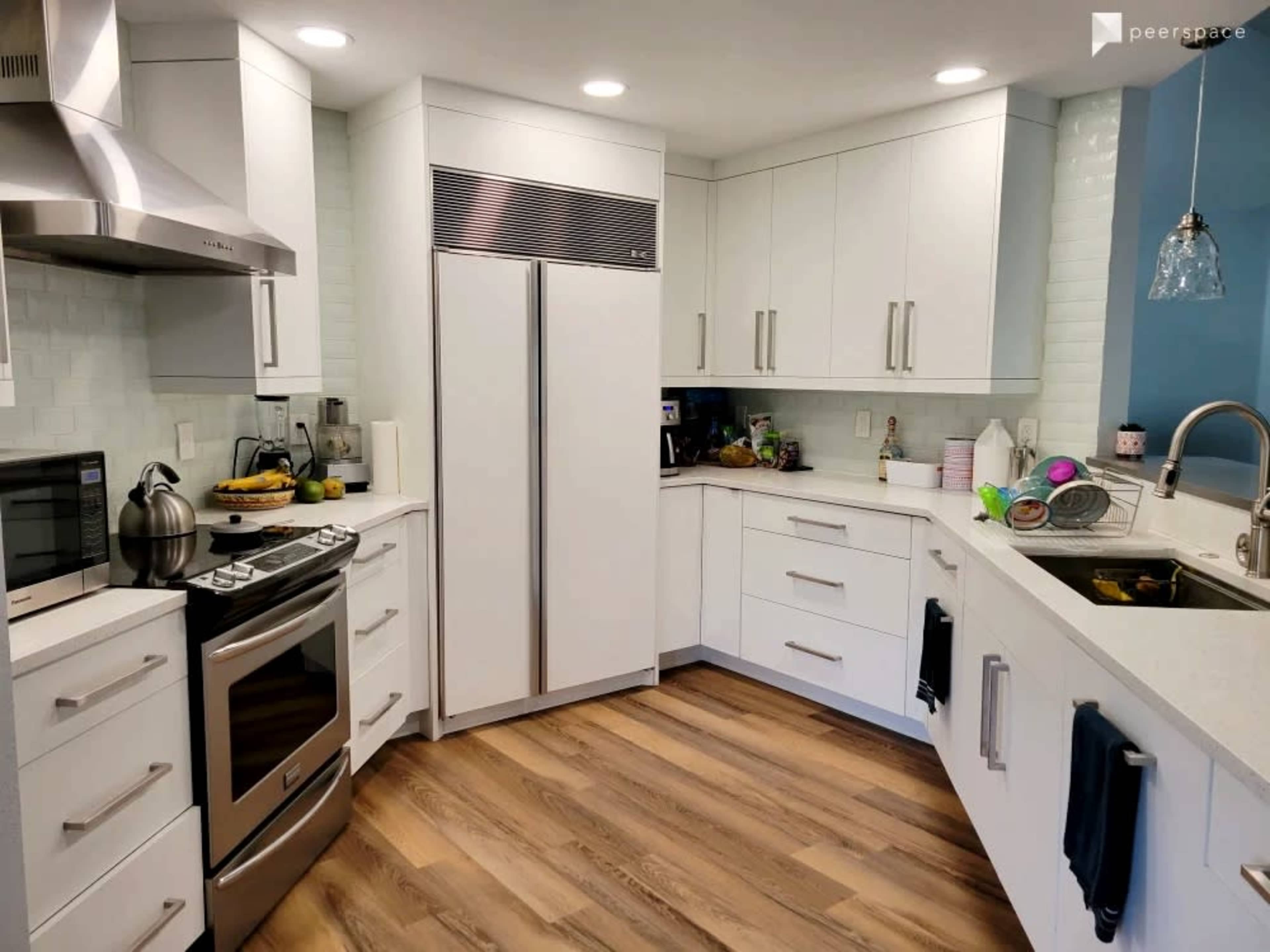 A modern kitchen with white cabinetry, stainless steel appliances, and wooden flooring.