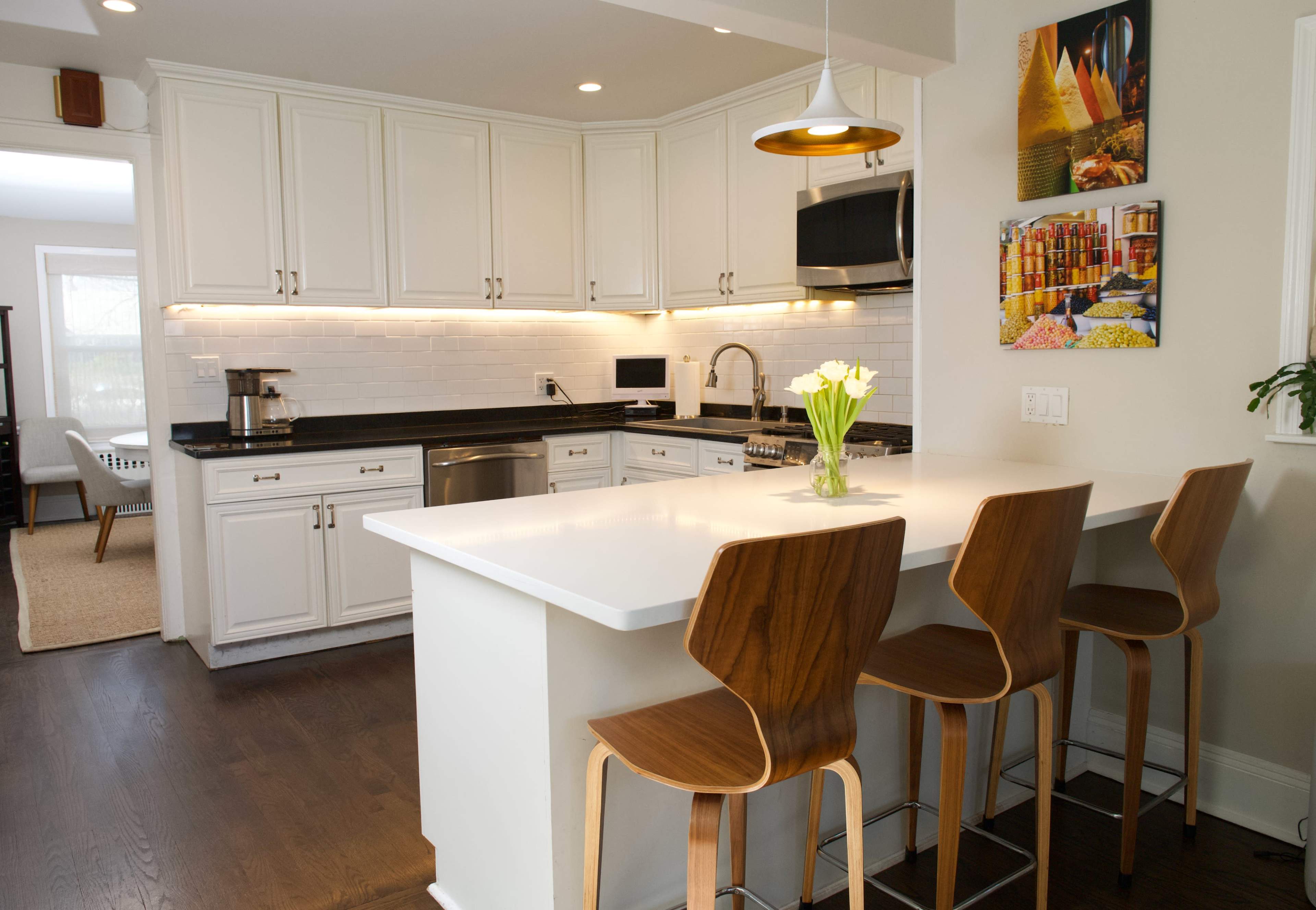 A modern kitchen features white cabinetry, a black countertop, and a breakfast bar with four wooden stools.
