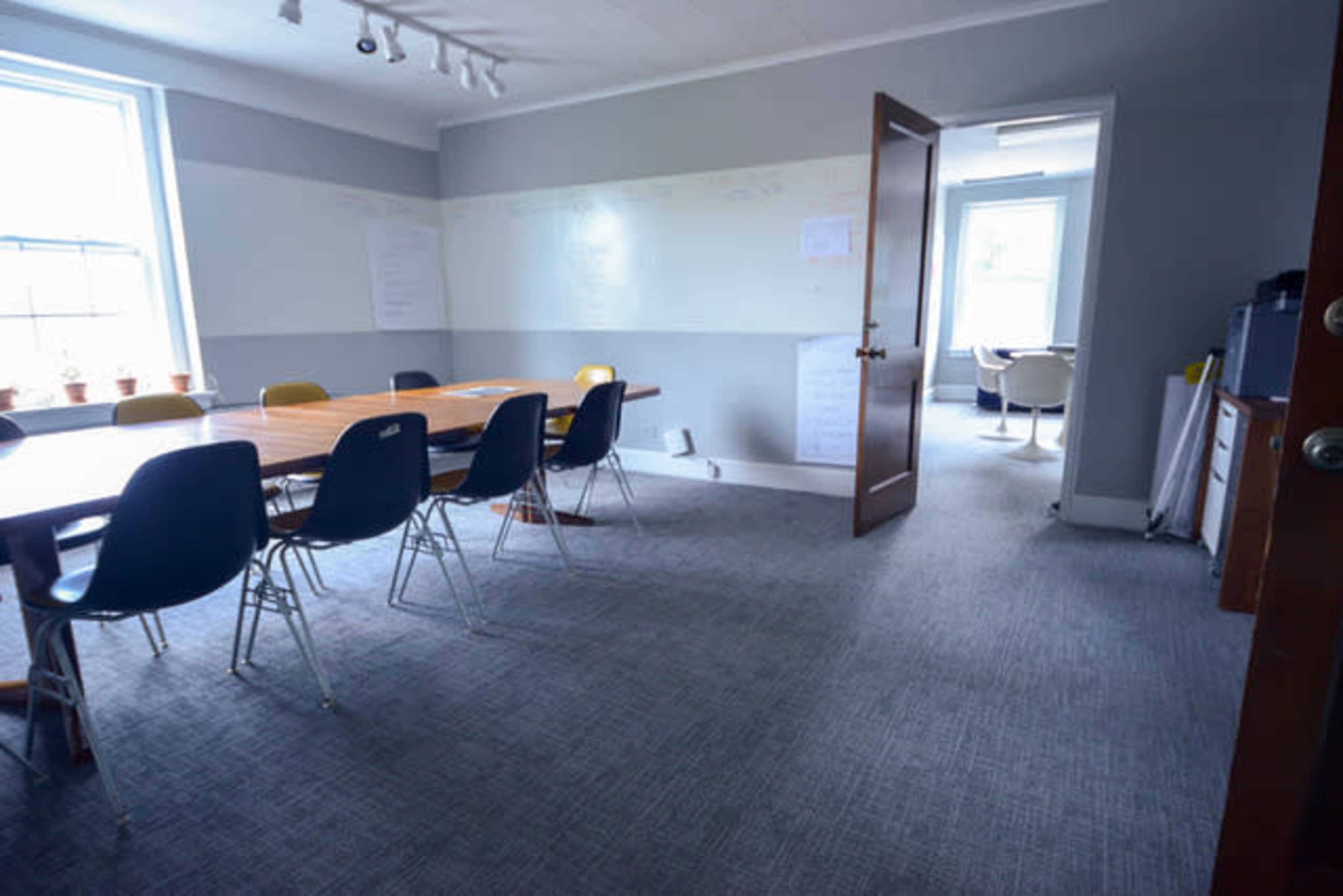 A conference room with a long table surrounded by chairs, and a doorway leading to an adjacent space.