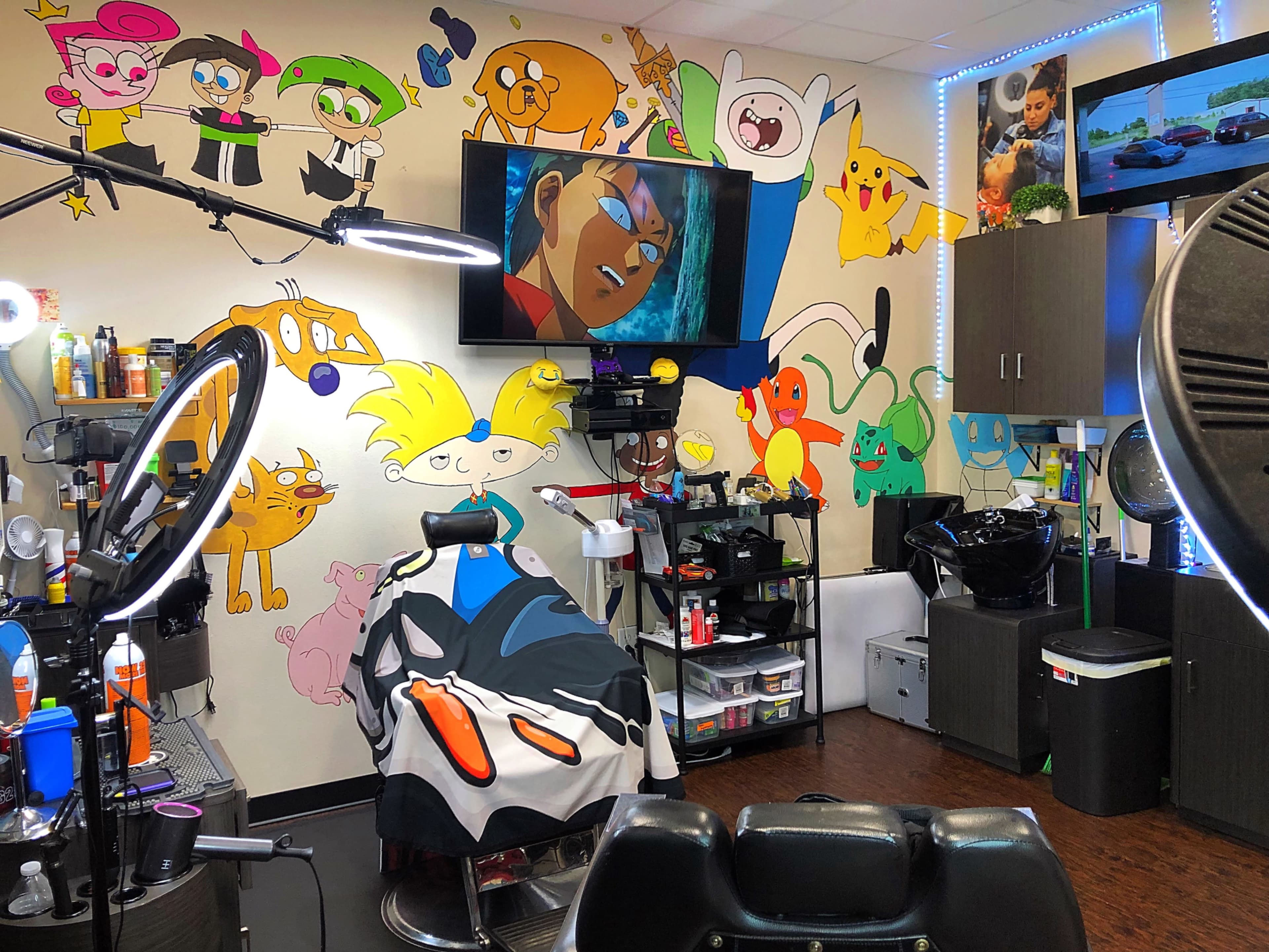 A brightly decorated barbershop with cartoon murals on the walls, a barber chair with a patterned cape, and various styling tools and products arranged on shelves.