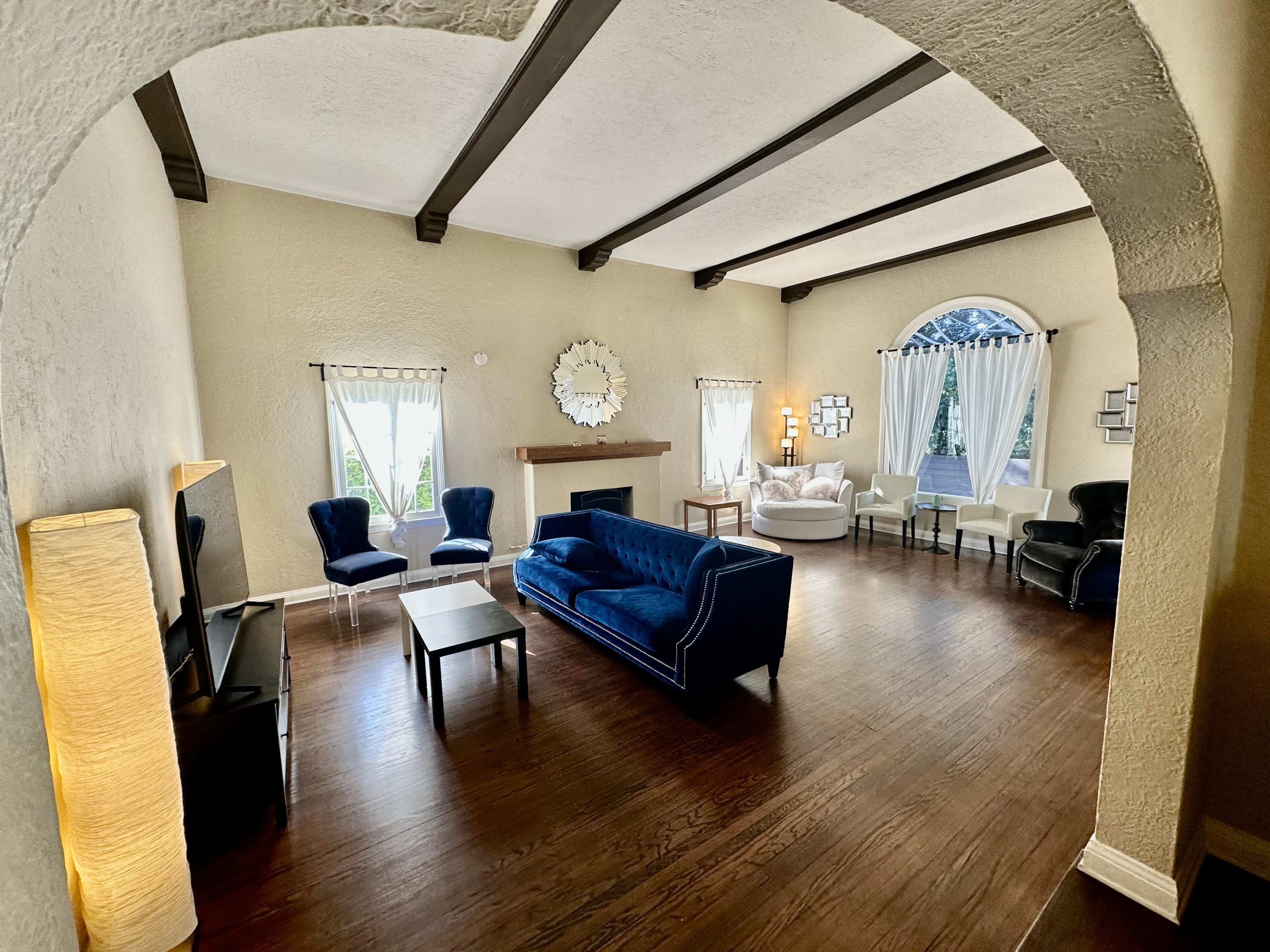 A spacious living room features a blue sofa, armchairs, and a coffee table, with large windows allowing natural light to enter.