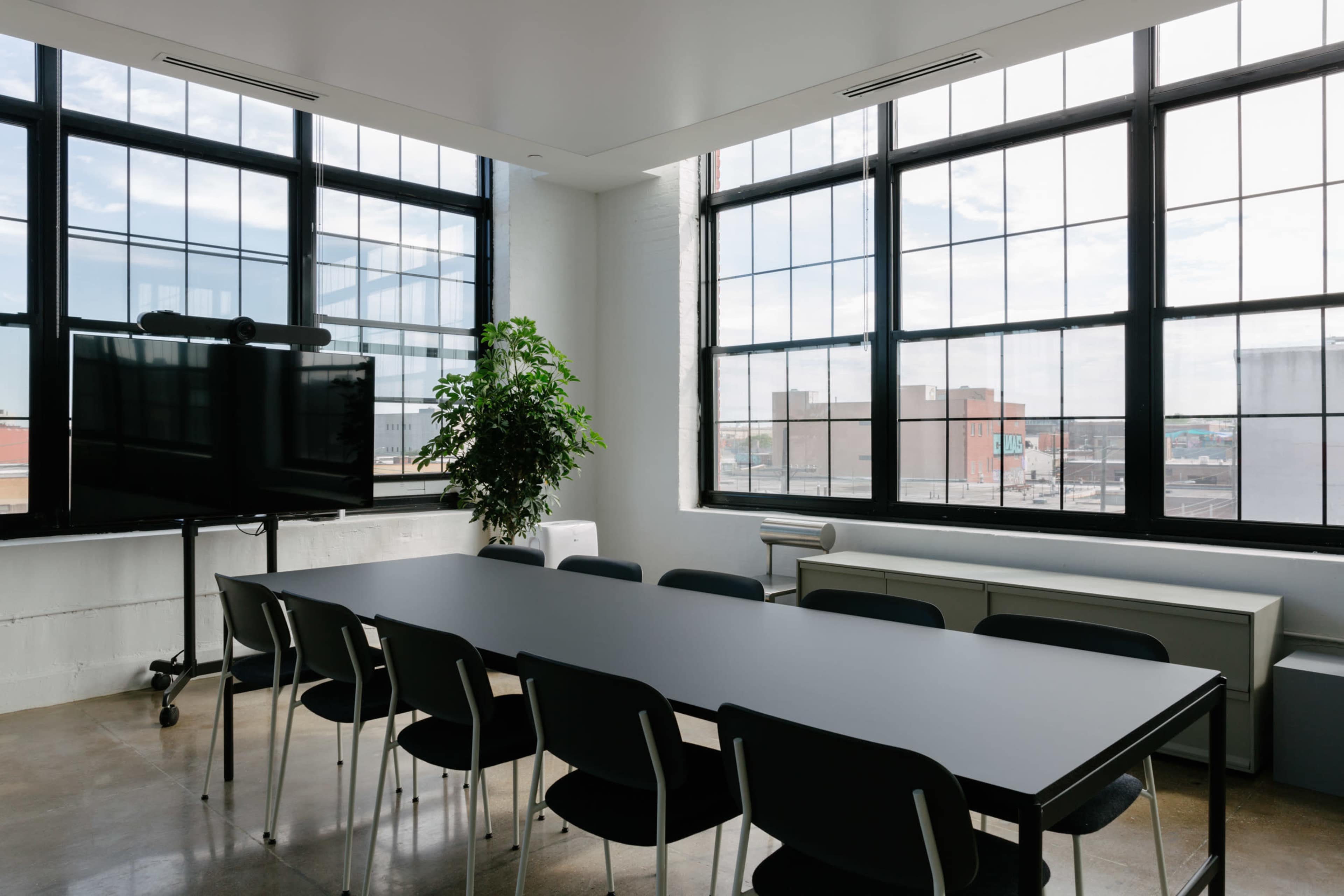 A modern conference room features a long black table surrounded by black chairs, with large windows allowing natural light to fill the space.