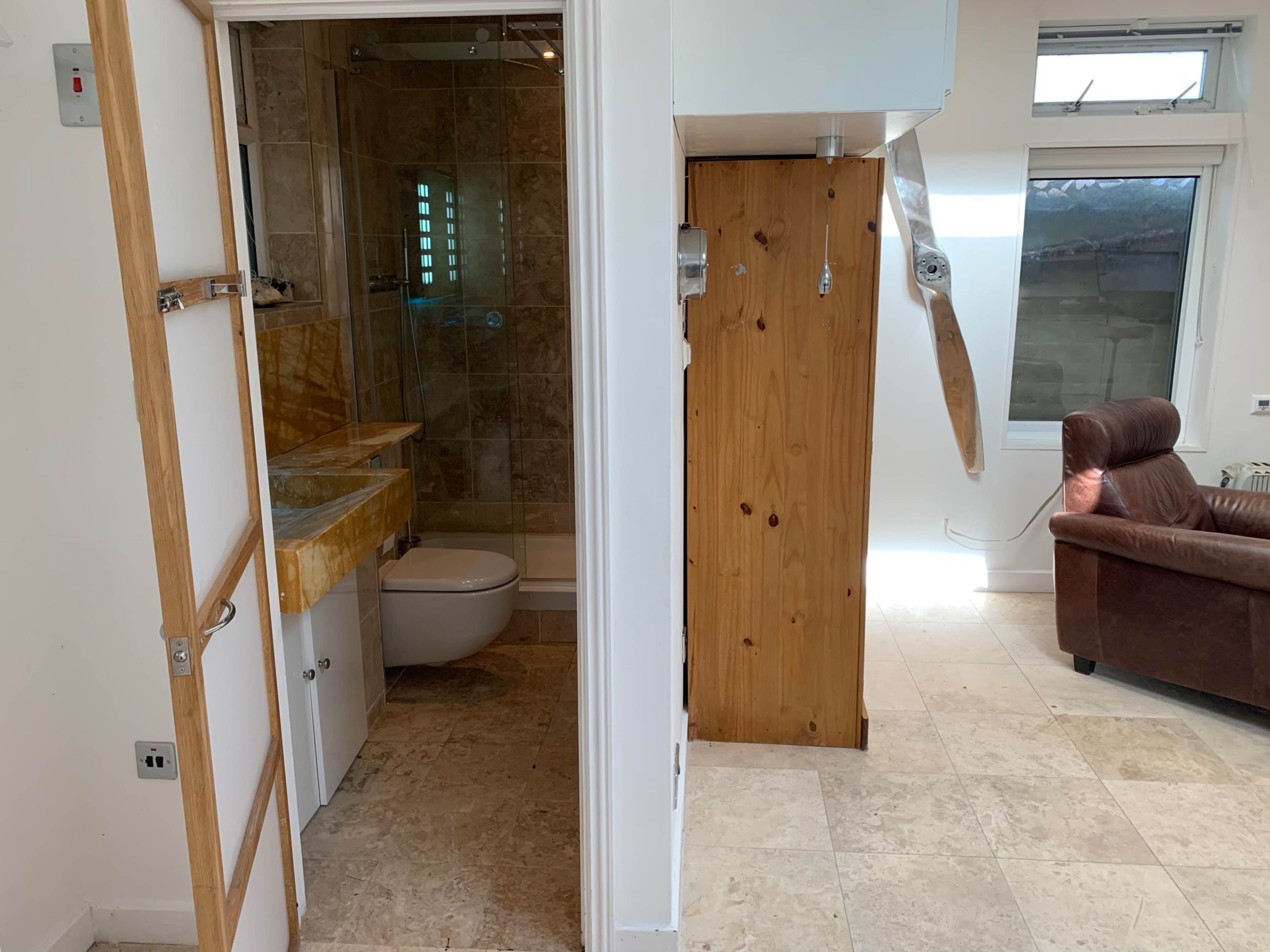 A bathroom on the left with a toilet and countertop, and a living area on the right featuring a leather couch and a wooden cabinet.