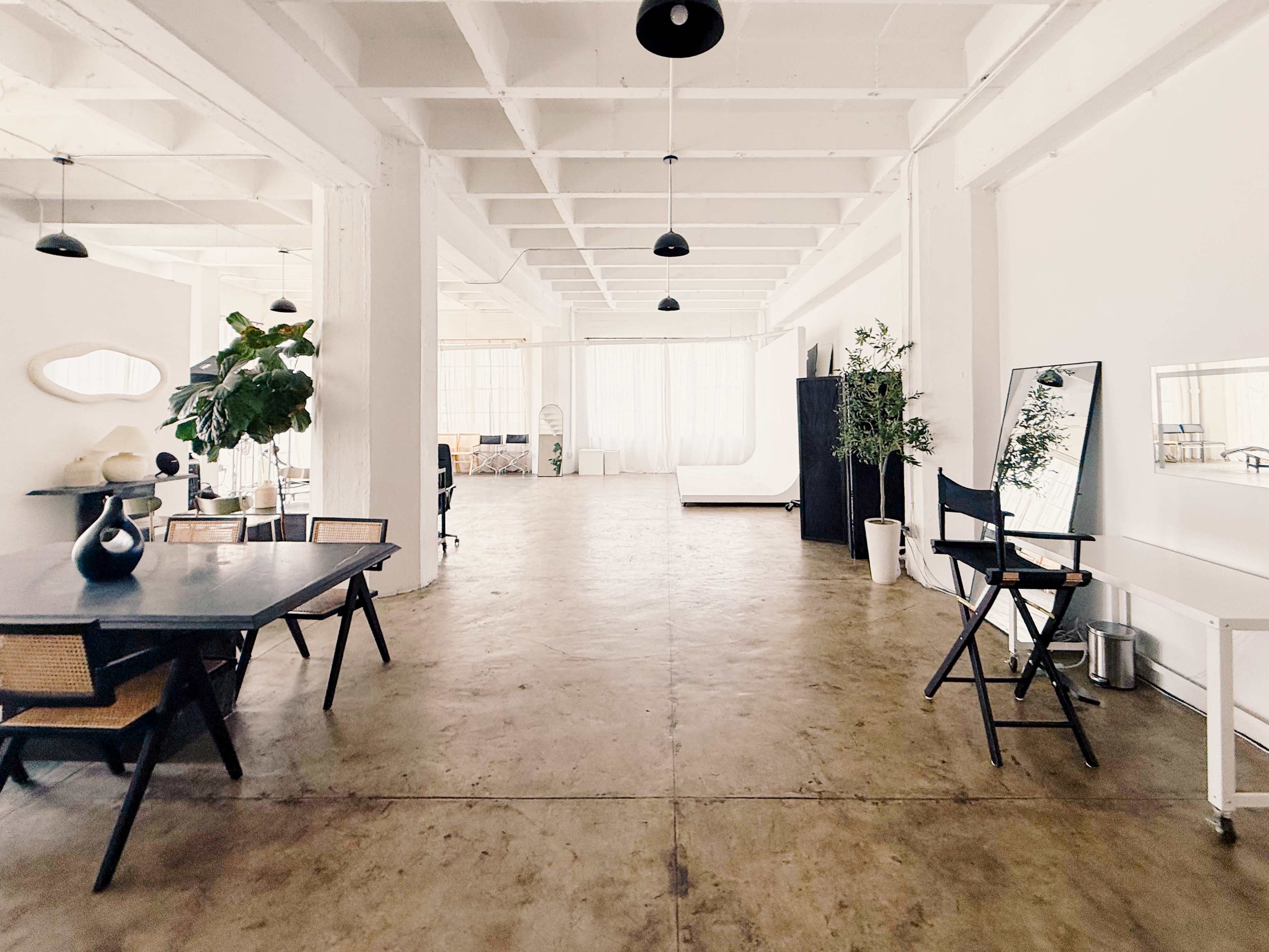 The image shows a spacious, minimalist interior with a large, empty room featuring concrete floors, white walls, and modern furniture.