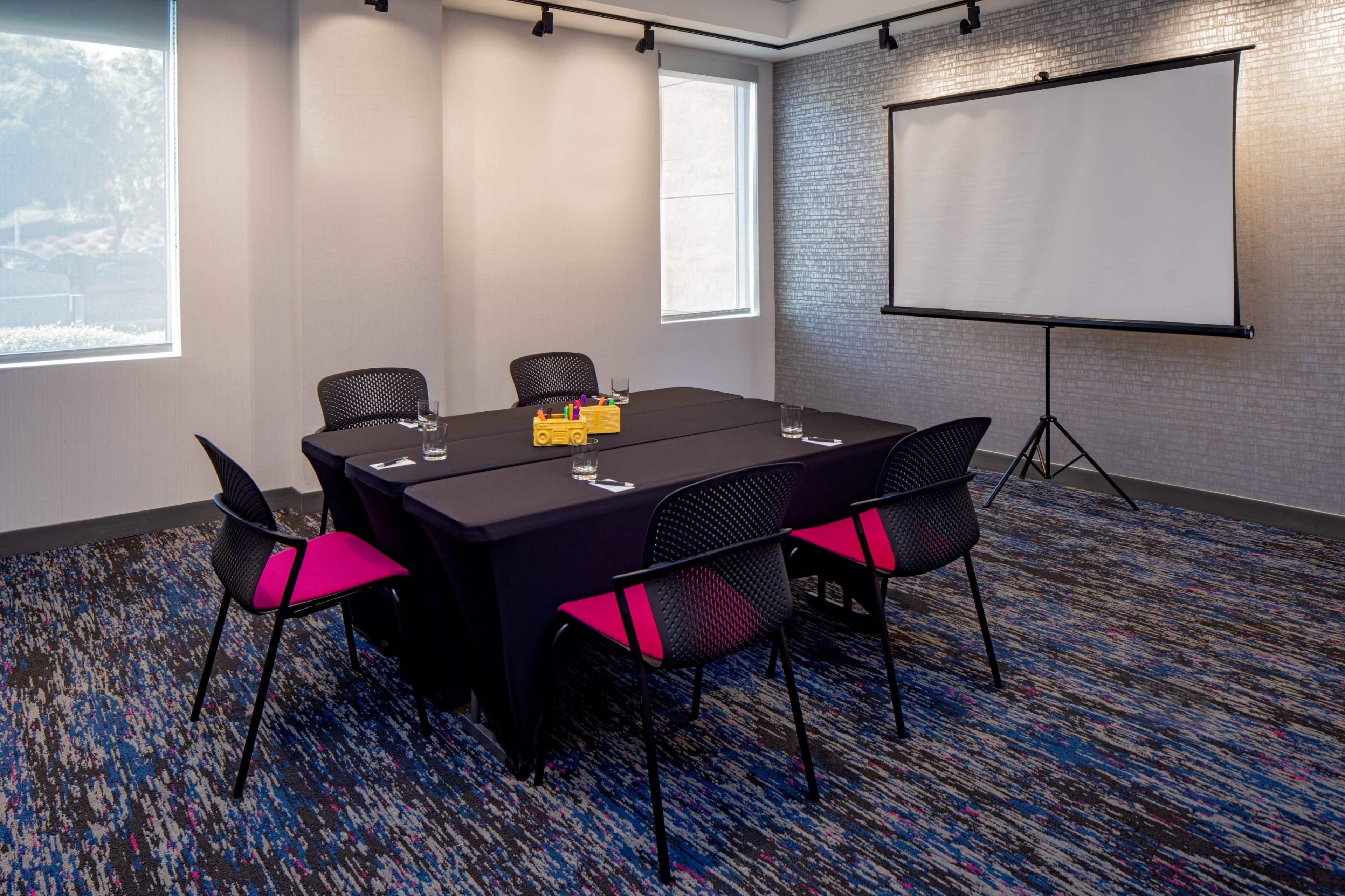 A conference room is set up with a black tablecloth covering a rectangular table surrounded by five chairs, with a projector screen positioned nearby.