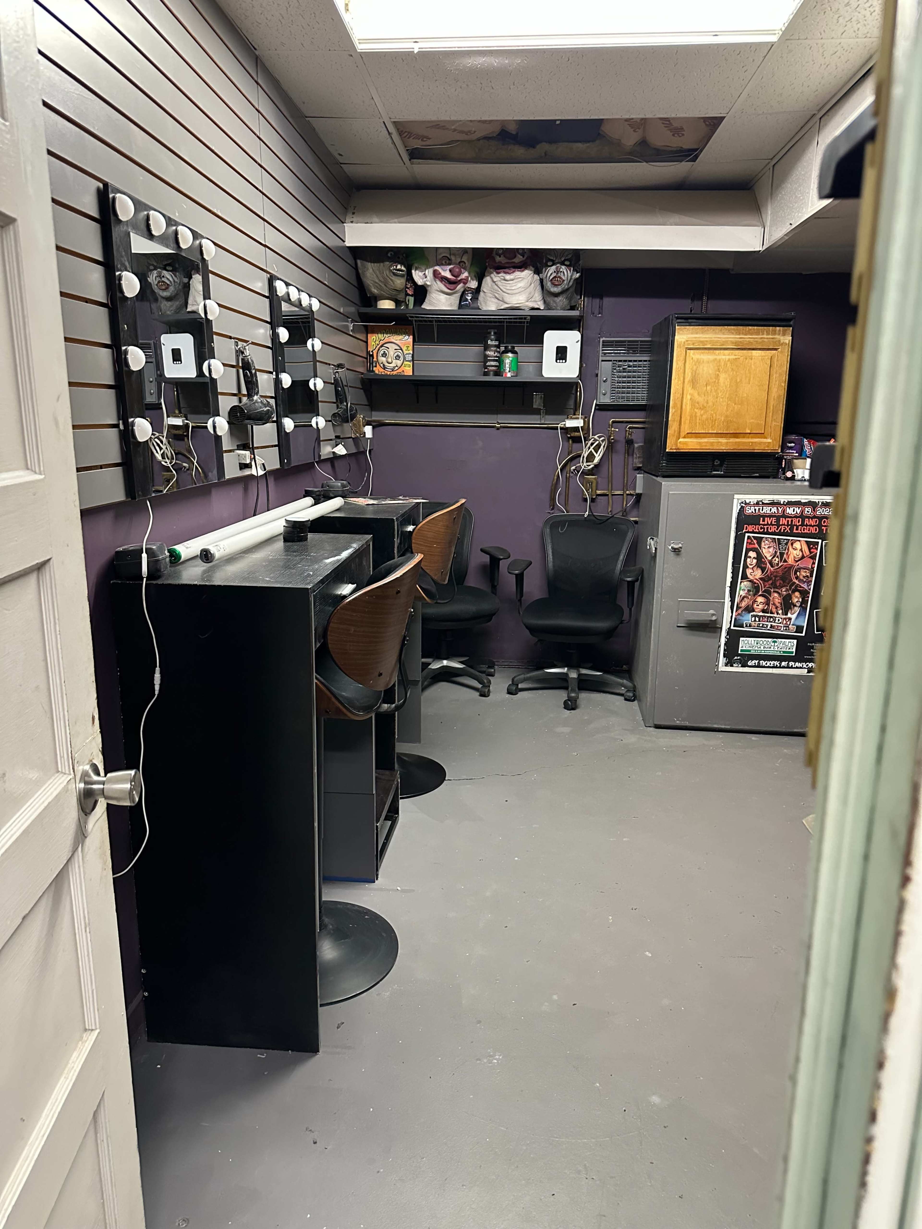 The image shows a small, dimly lit room with two chairs and a desk against the walls, featuring several mirrors and a cabinet in the corner.