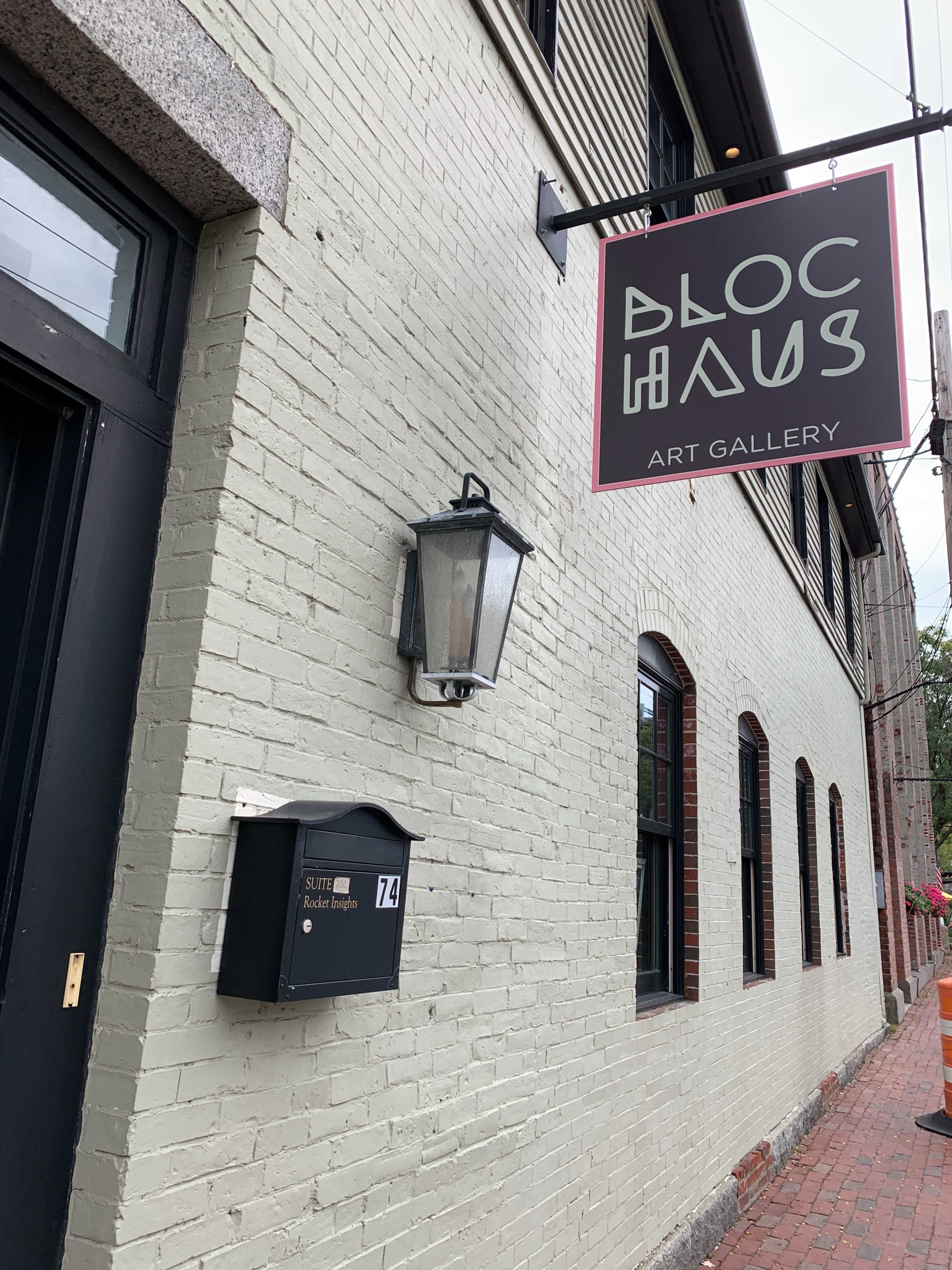 The exterior of an art gallery named "Bloc Haus," featuring a sign and a mailbox mounted on a light-colored brick wall.