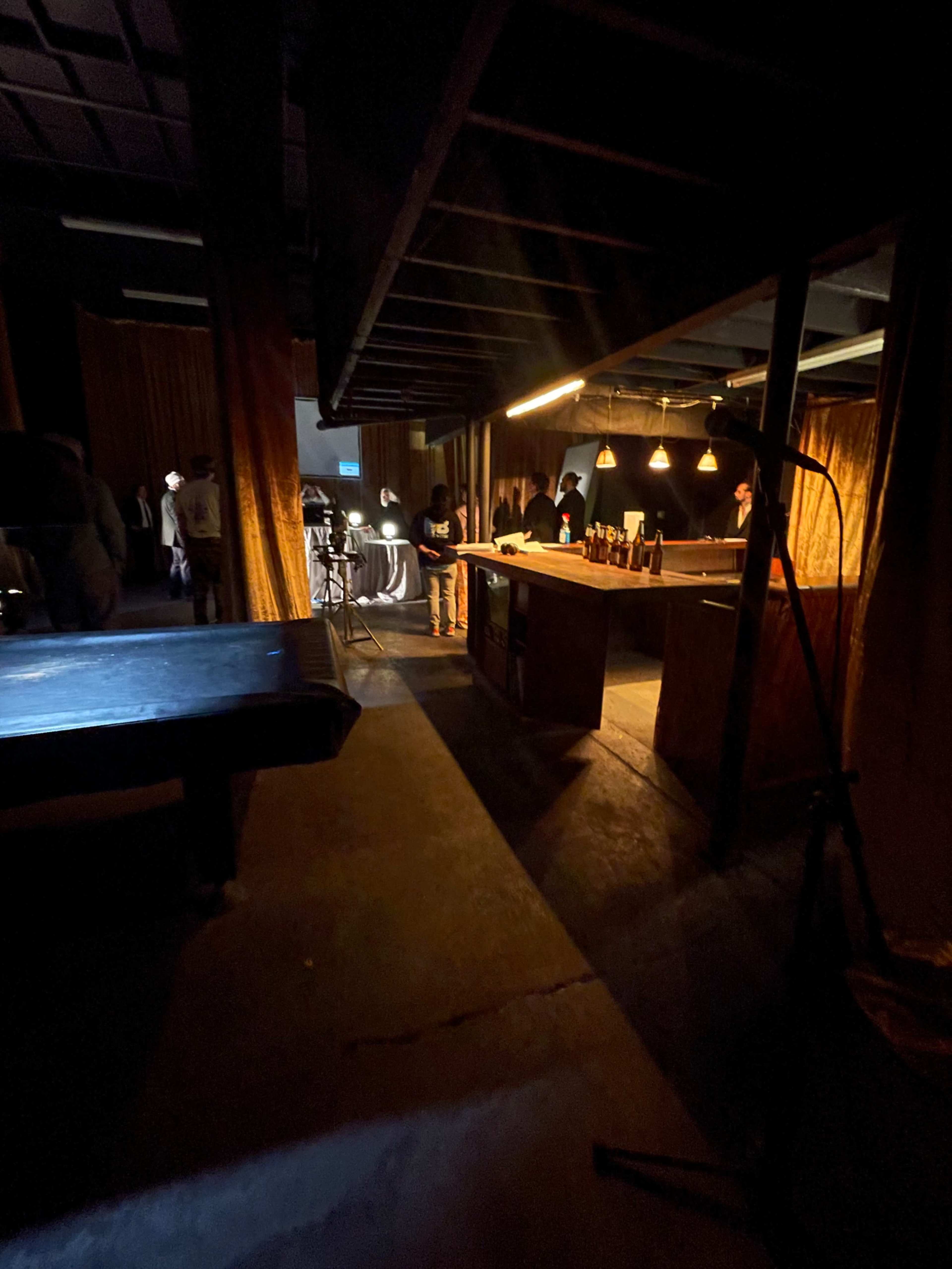 The image shows a dimly lit interior space with a bar area, tables, and a pool table, where several people are engaged in activities under warm lighting.