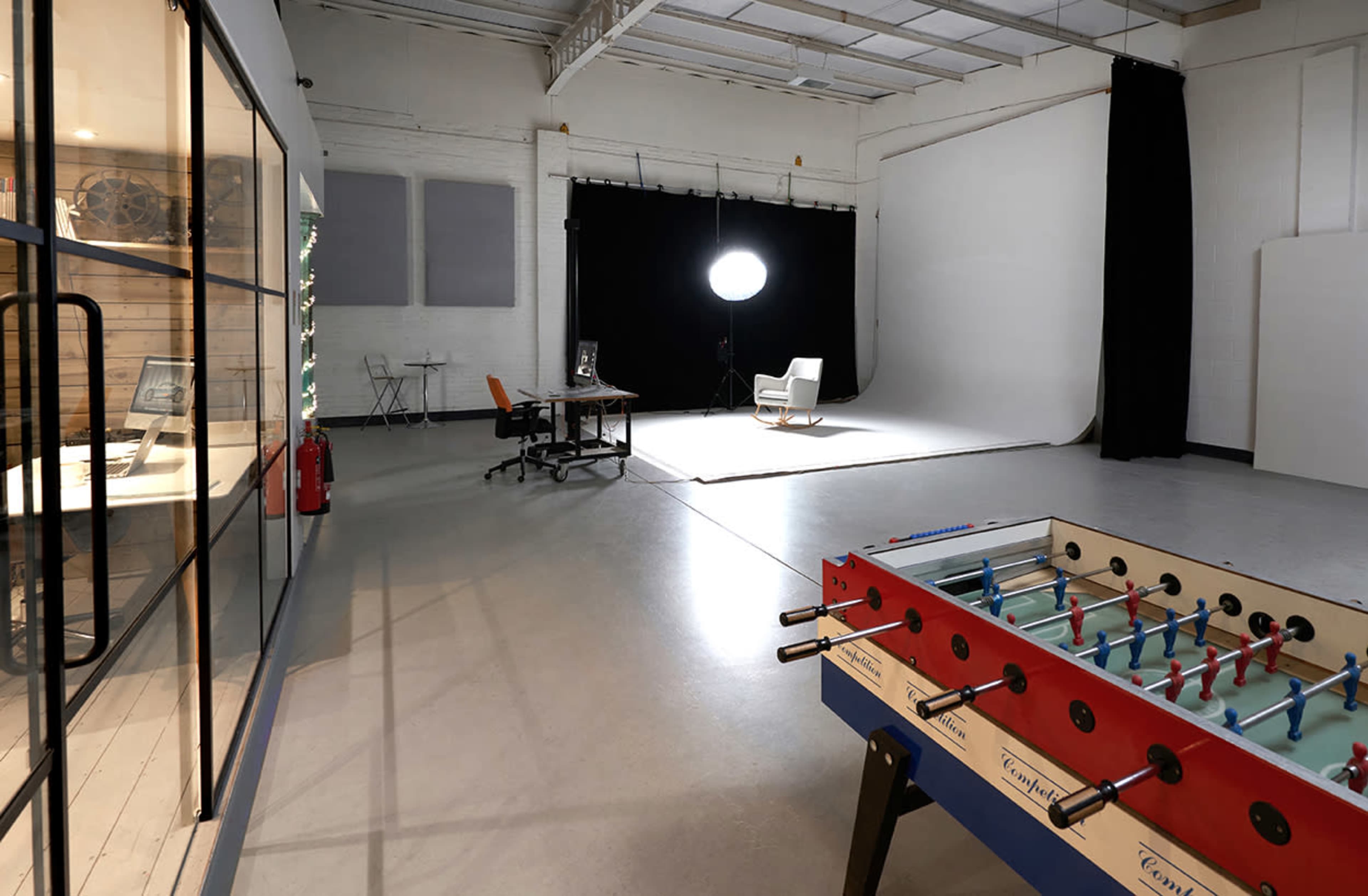 A spacious studio with a foosball table, a desk with a computer setup, and a large backdrop for photography.