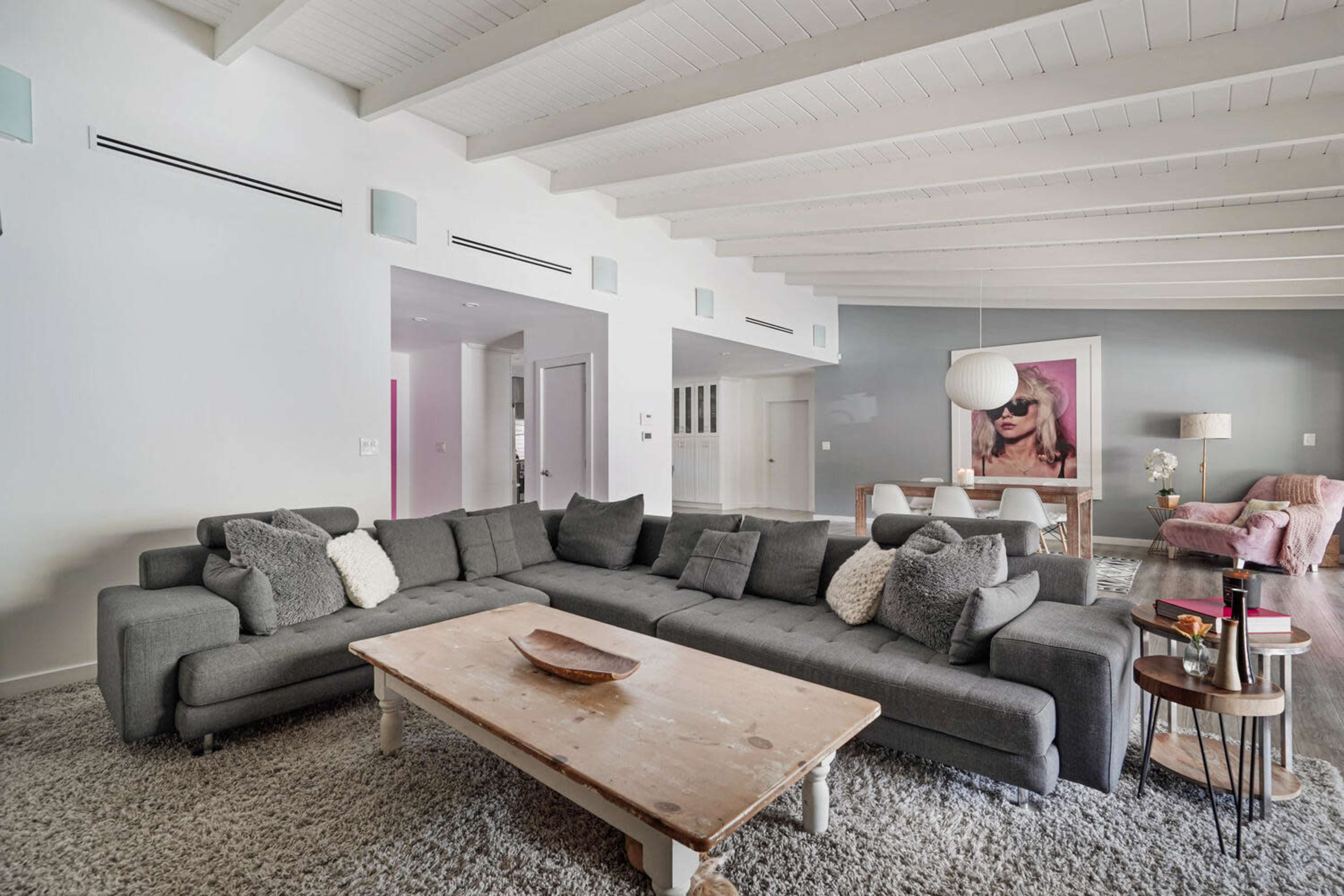 A spacious living room with a large gray sectional sofa, a wooden coffee table, and a dining area in the background, featuring soft lighting and modern decor.