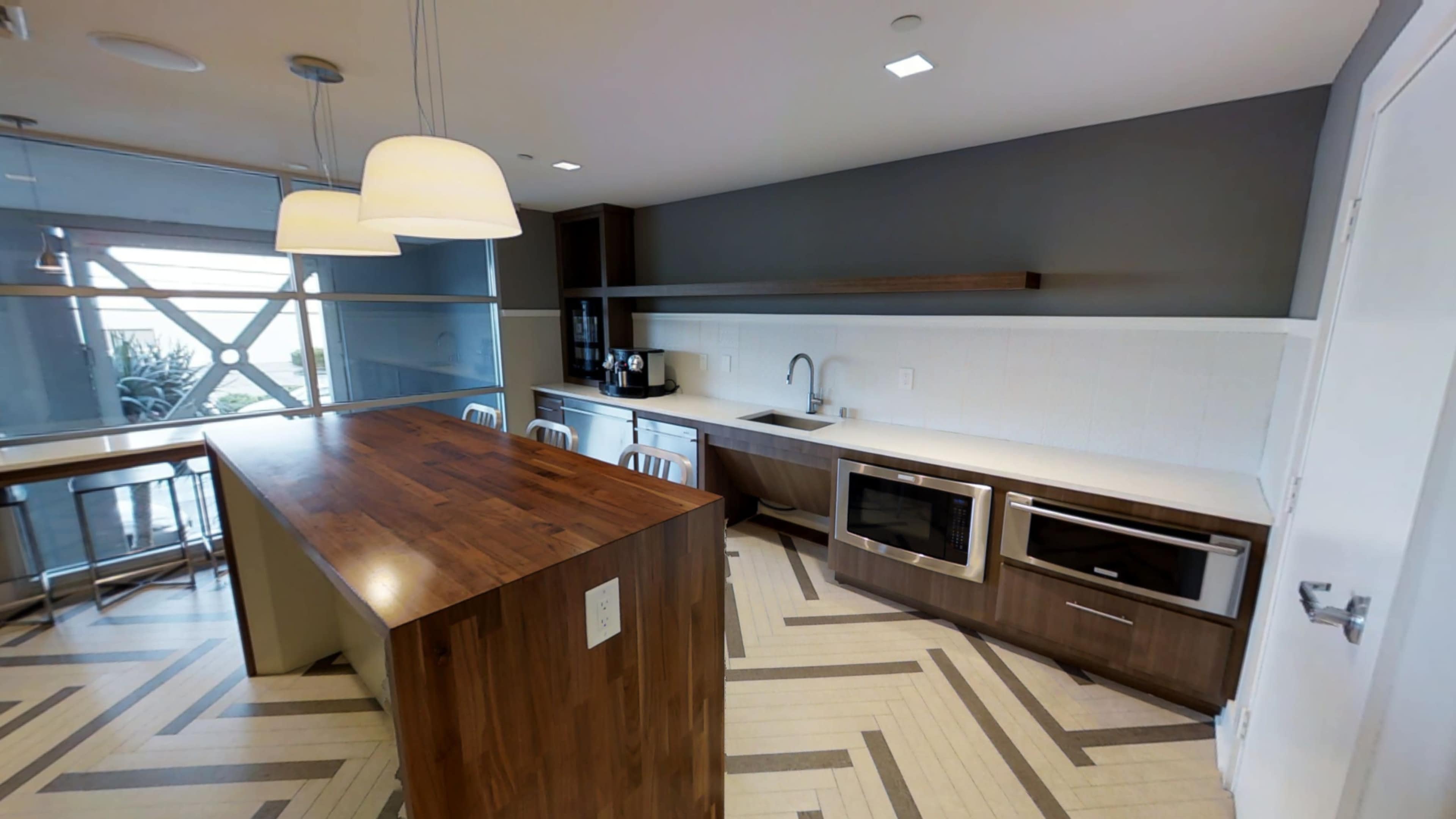 The image shows a modern kitchen featuring a large wooden island, stainless steel appliances, and a minimalist design with light-colored cabinetry.