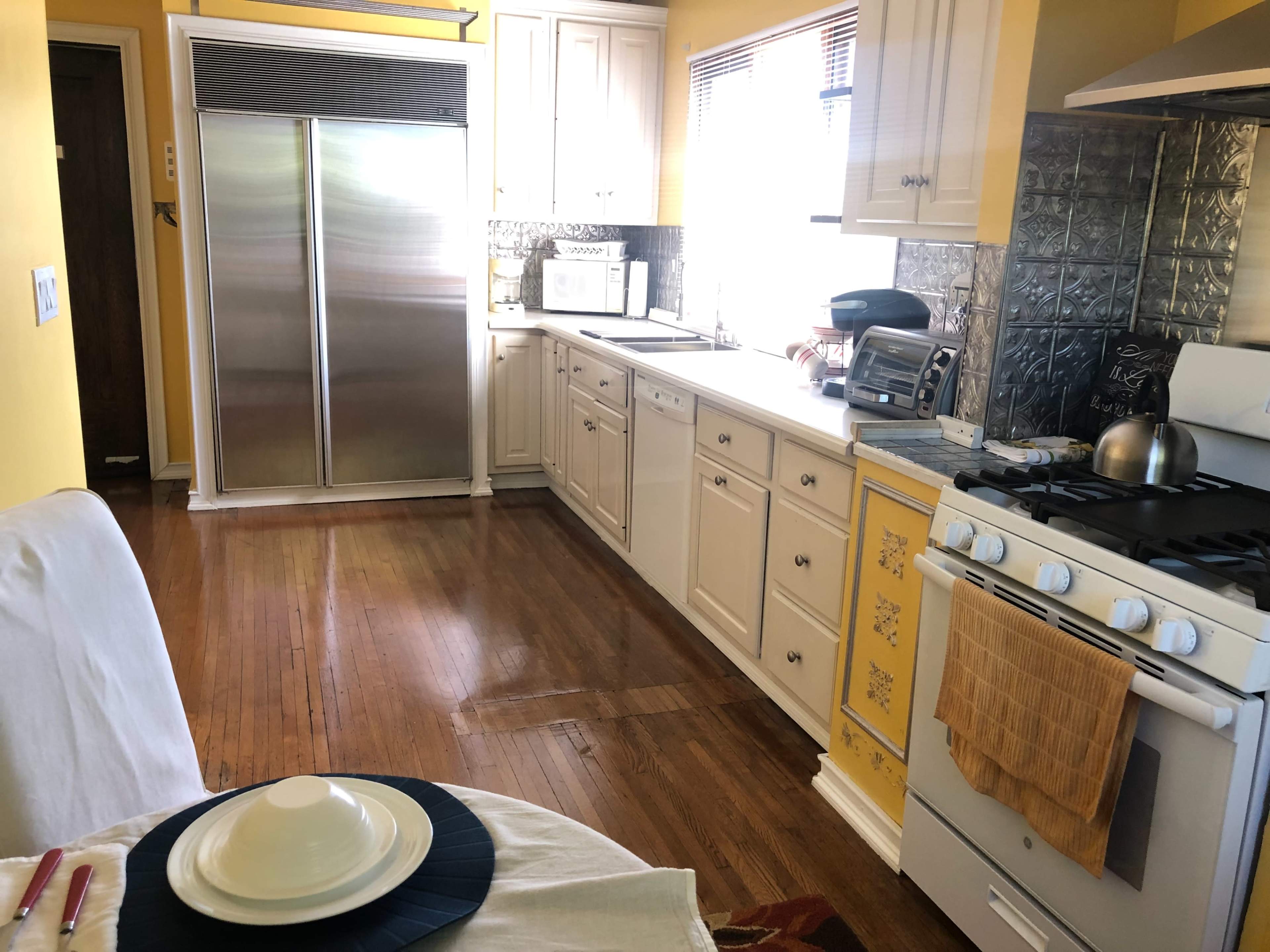 A kitchen featuring yellow walls, wooden floors, a stainless steel refrigerator, and white cabinetry with a gas stove on the right.