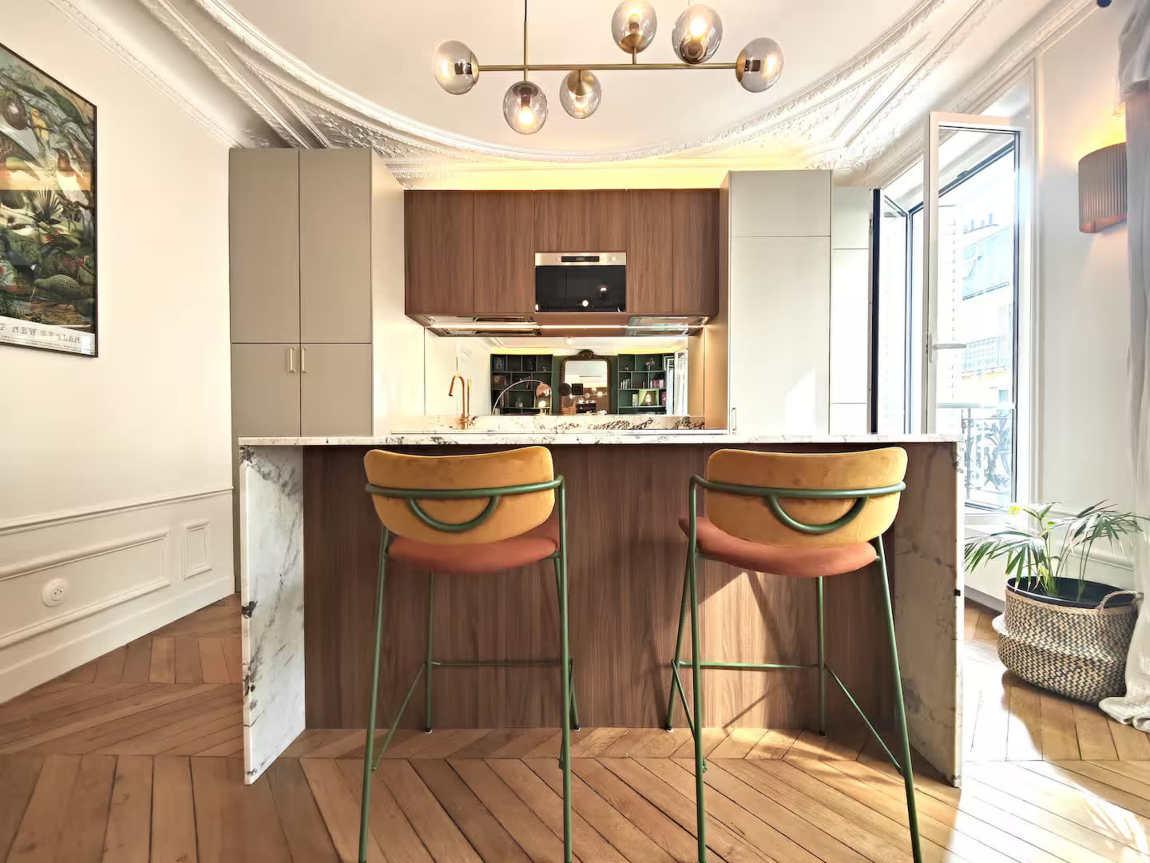 A modern kitchen features a marble-topped island with two bar stools and large windows that illuminate the space.