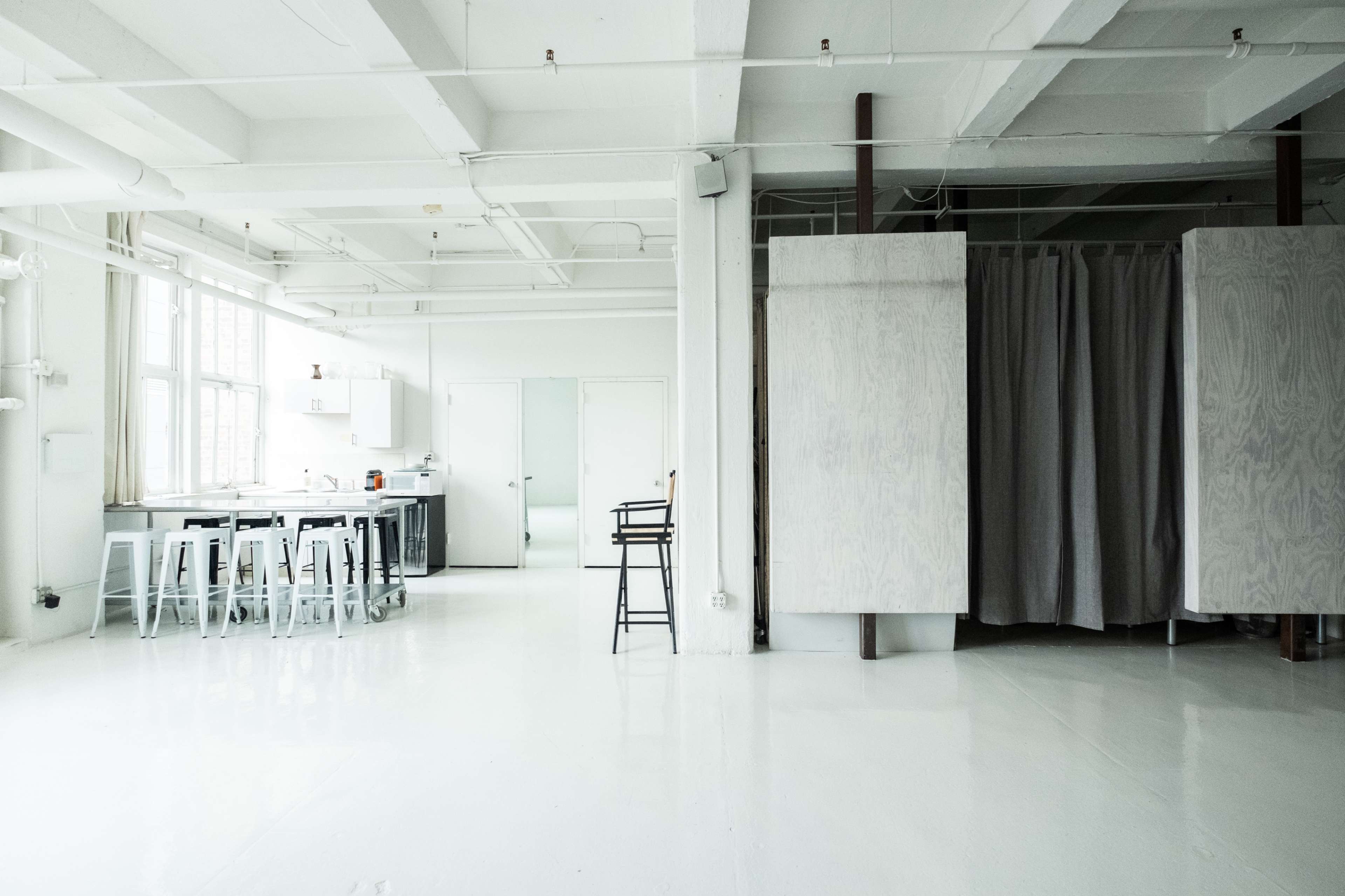 The image shows a spacious, modern studio with a kitchen area on one side and a set of curtains separating a section of the room.