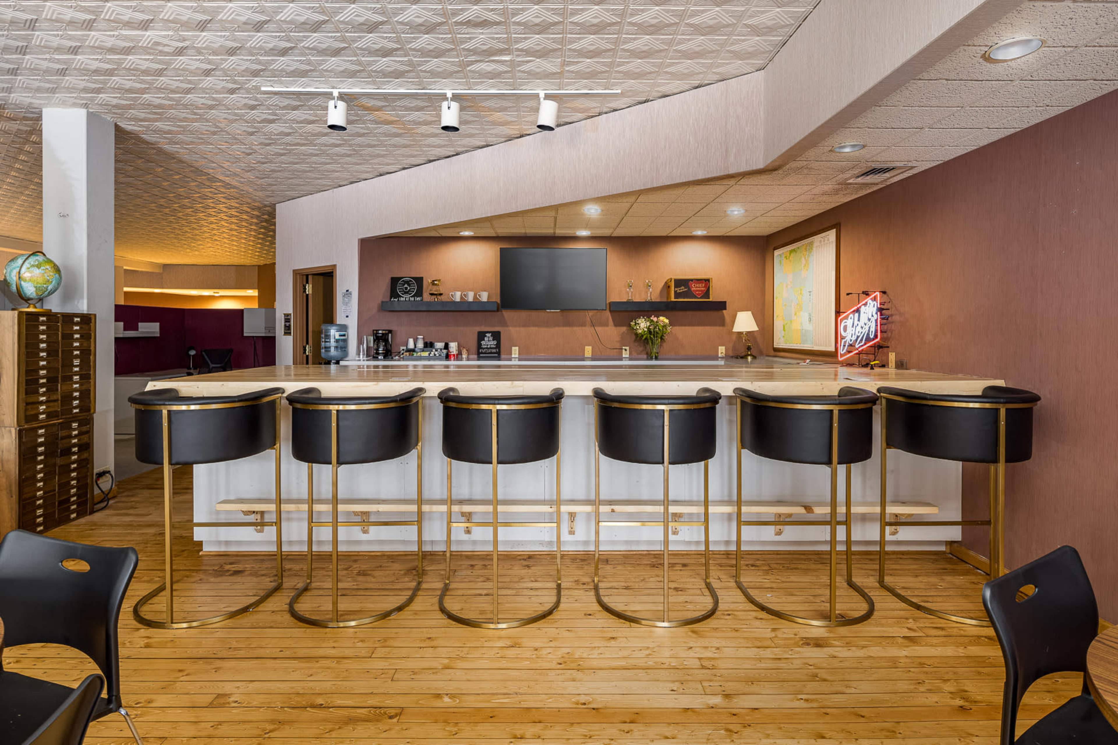 A contemporary bar area featuring a light-colored countertop with black and gold bar stools arranged in front of it, set against a backdrop of warm wooden flooring.