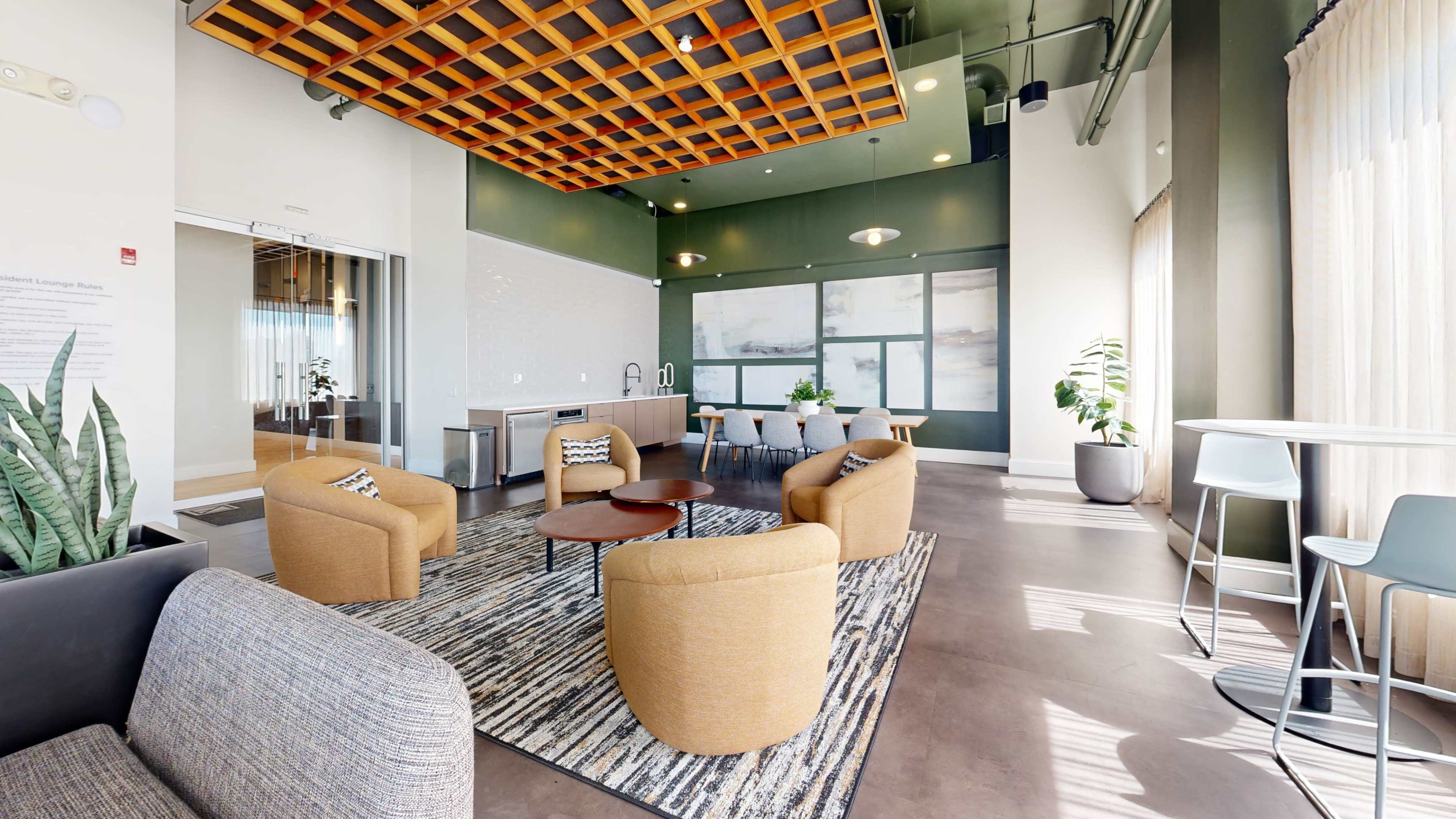 The image shows a modern lounge area with several round tables, seating arrangements, and a large window allowing natural light to enter.