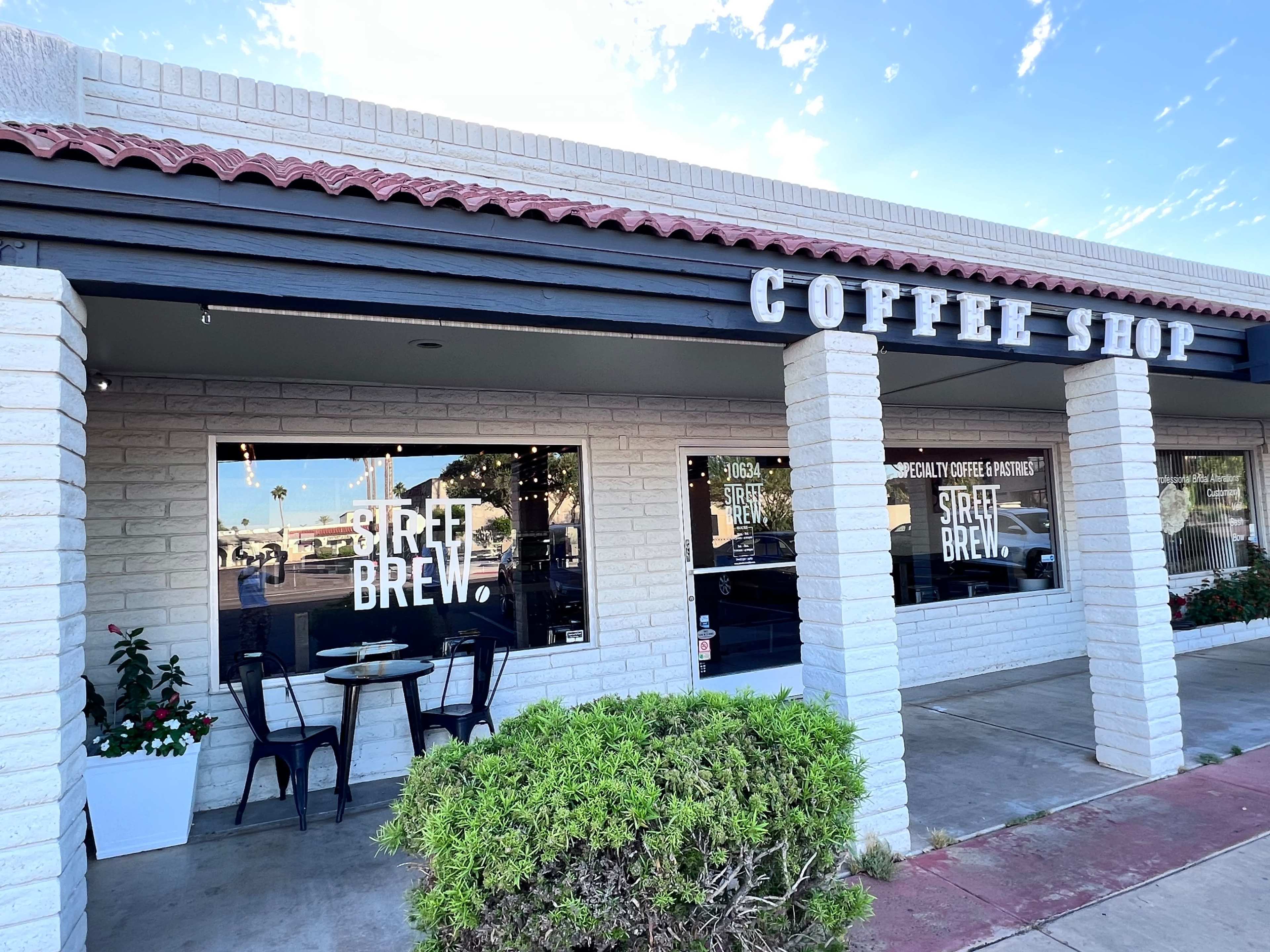 A coffee shop with a sign reading "COFFEE SHOP" above a storefront featuring large windows and outdoor seating.
