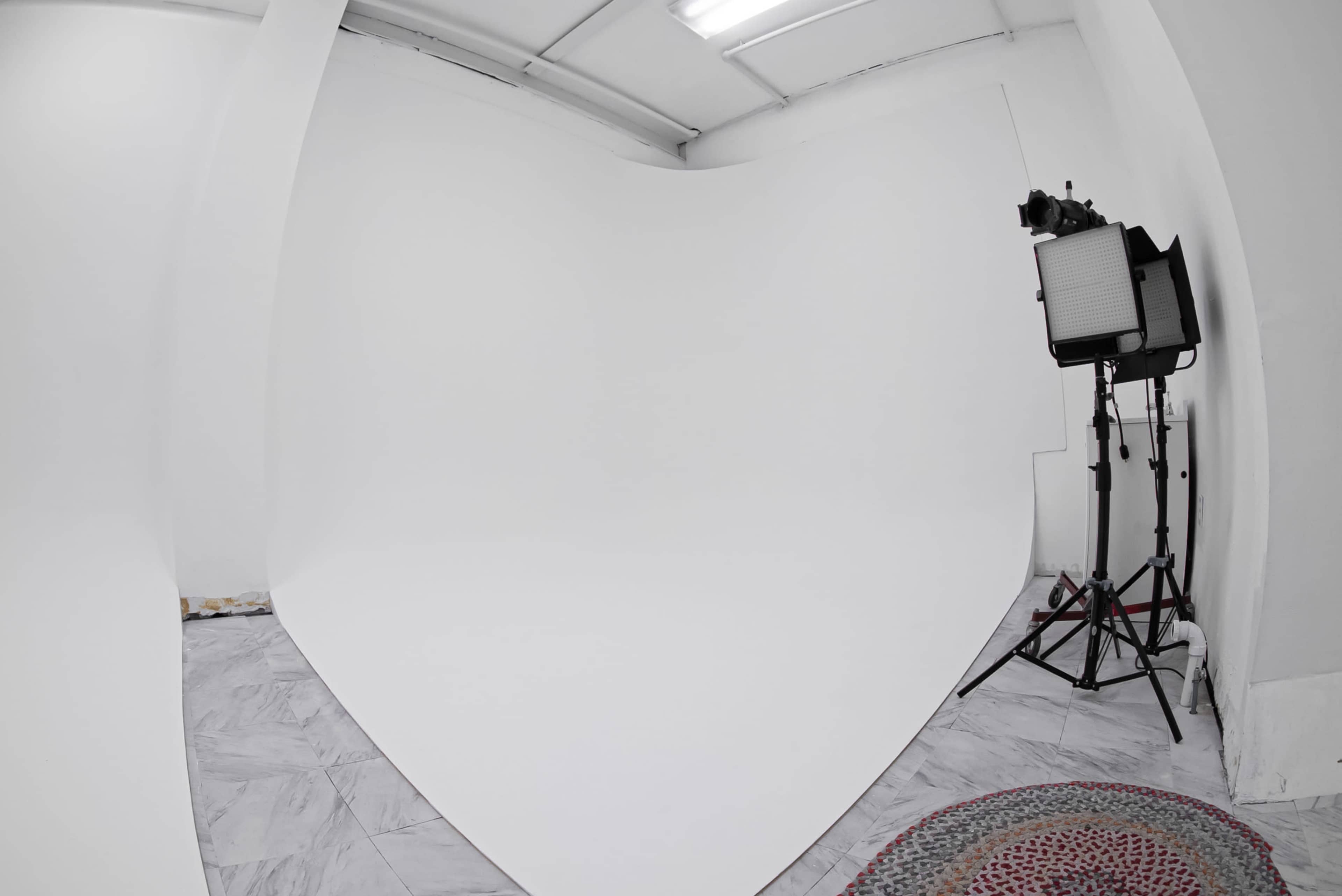 The image shows a spacious photography studio with a large white backdrop and a lighting setup in the corner.