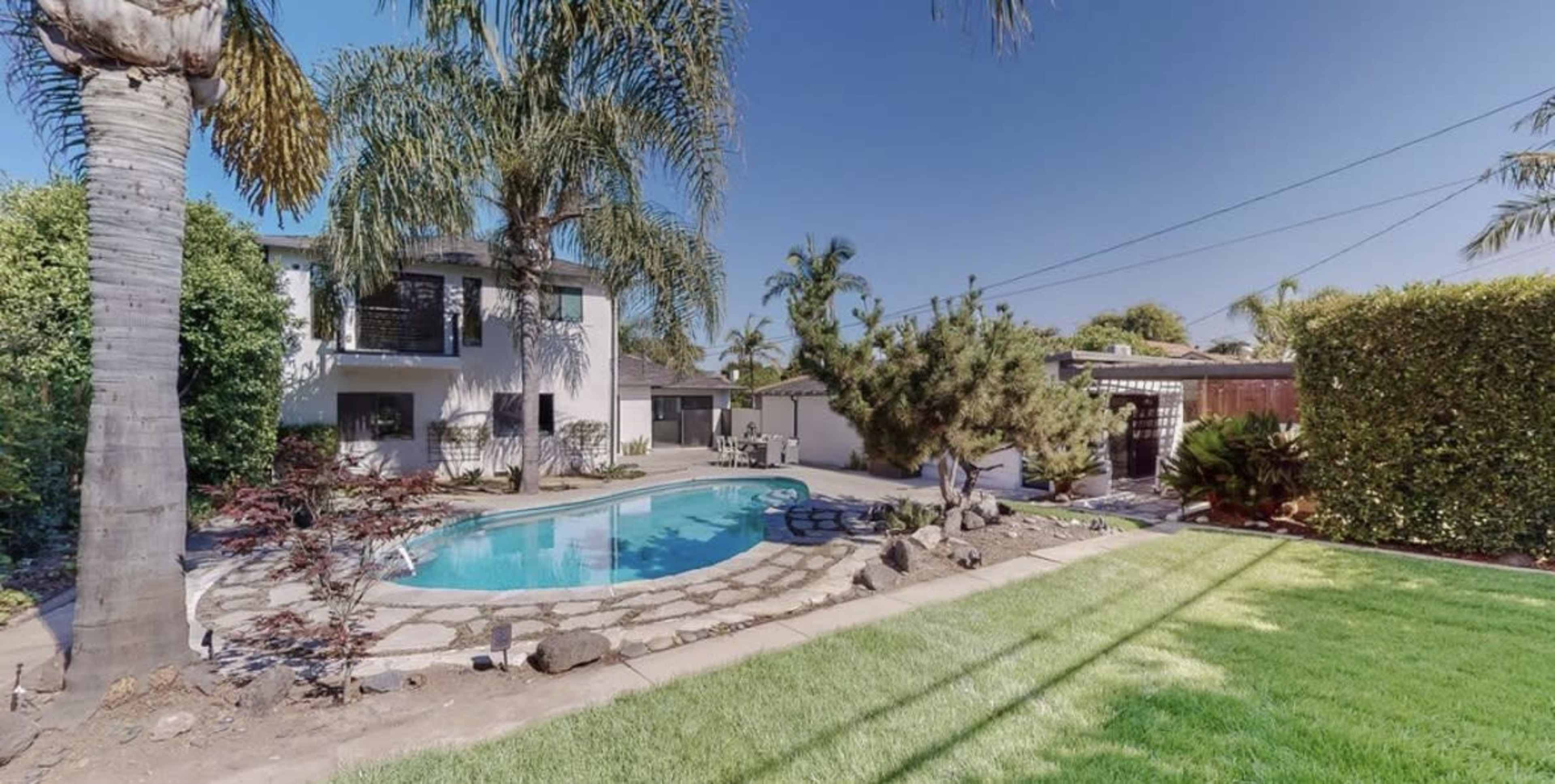 The image shows a residential backyard with a swimming pool, palm trees, and a well-maintained lawn.