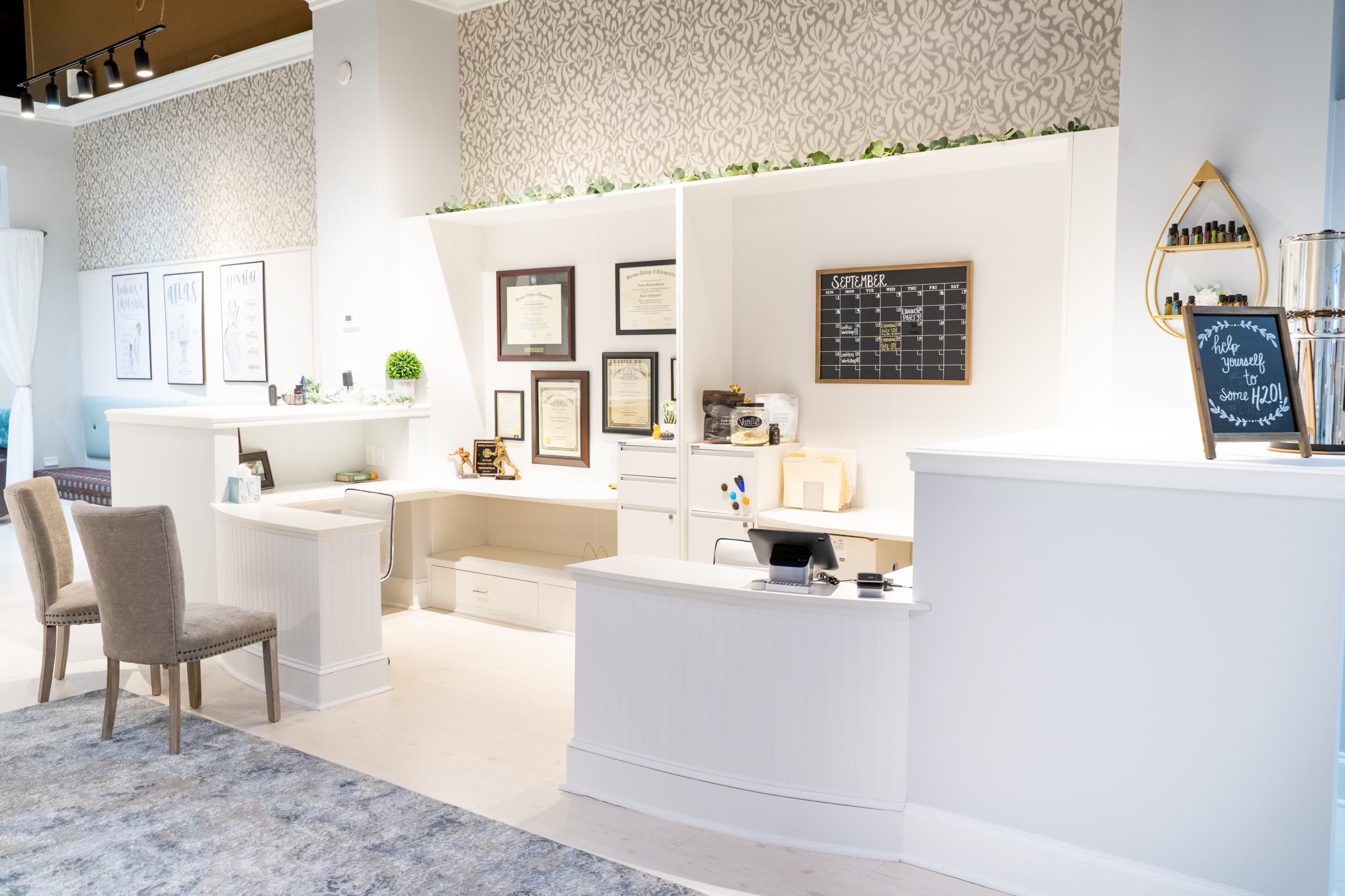 A modern reception area with a white front desk, framed certificates on the wall, and a decorative chalkboard.