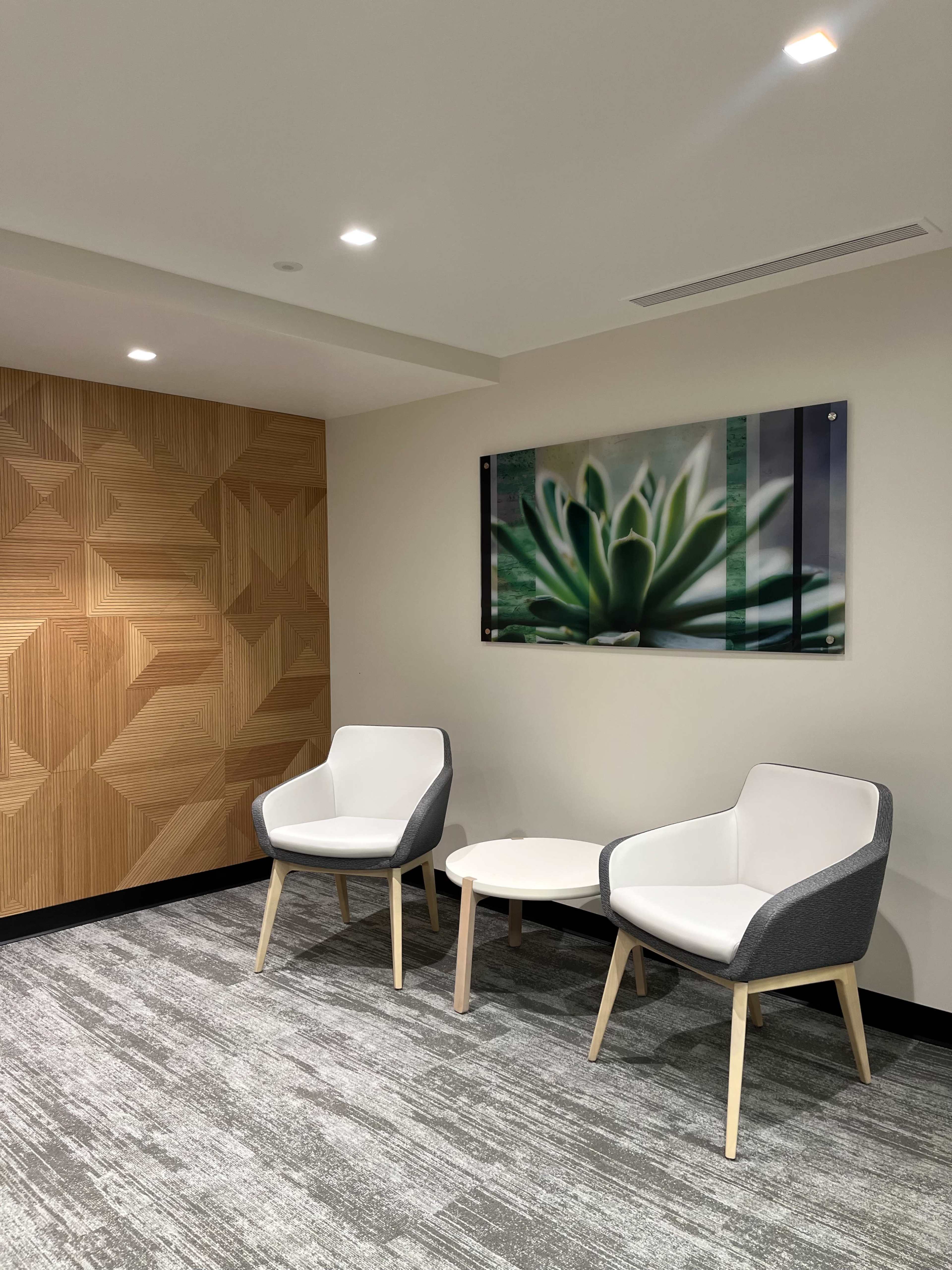 A small seating area featuring two modern chairs and a round table, with a patterned wall and a framed artwork of a plant.