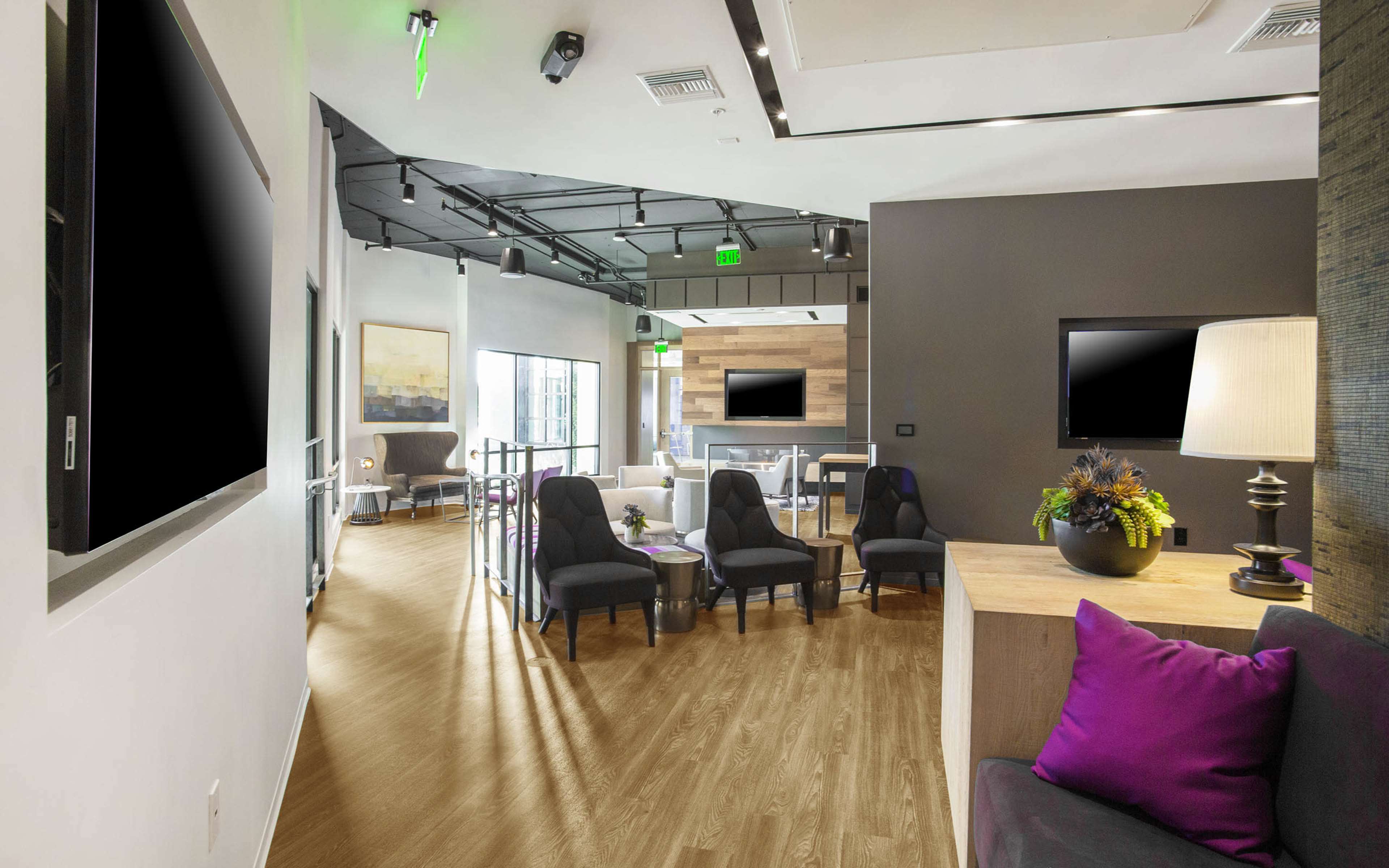 A modern lounge area with dark chairs, a wooden table, and large wall-mounted screens.