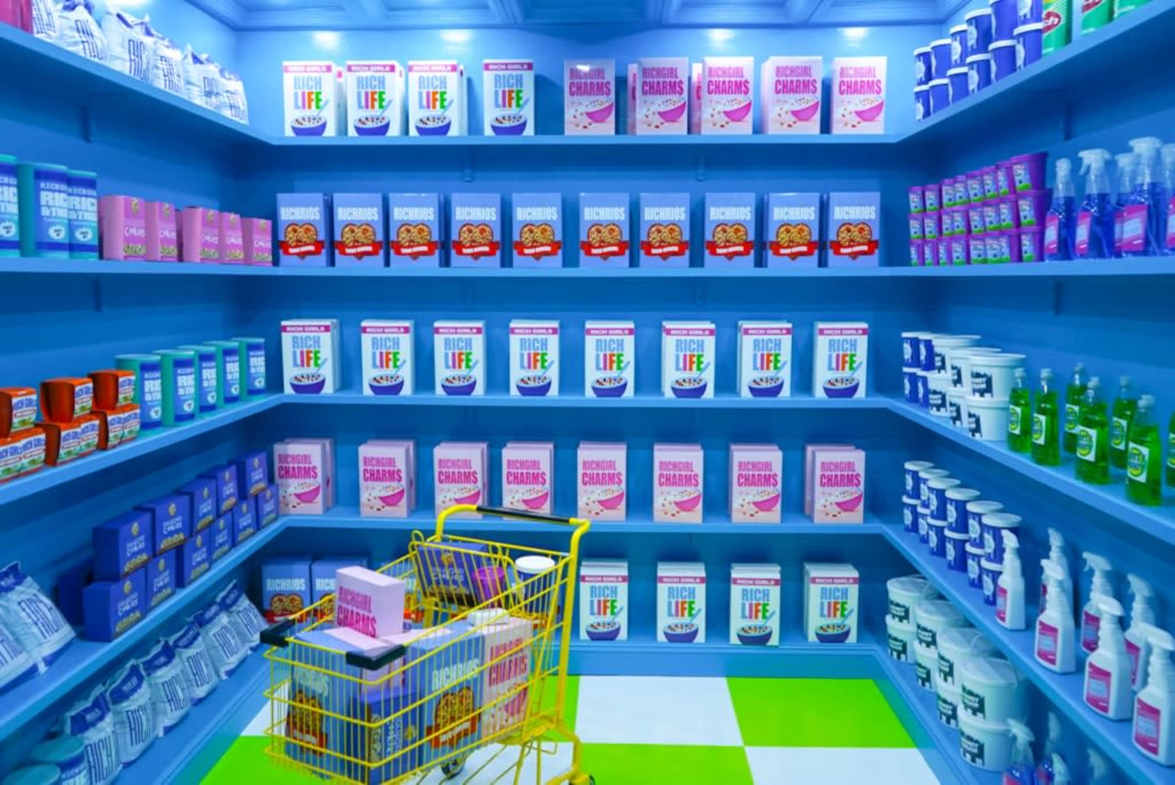 An aisle in a brightly colored store, filled with neatly arranged shelves of various boxed products and cleaning supplies, alongside a yellow shopping cart.