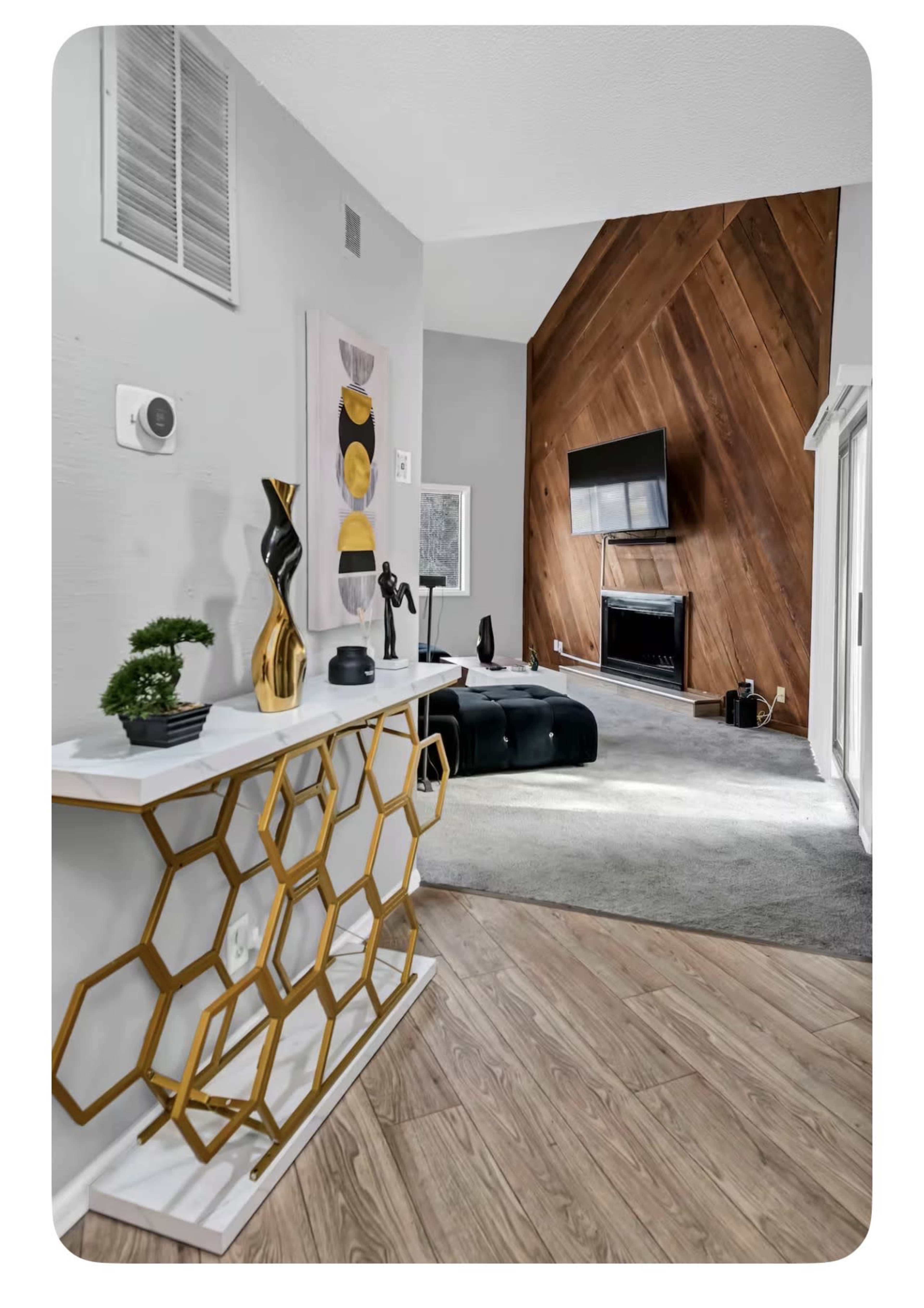The image shows a well-lit living room featuring a modern console table with a geometric design, a mounted television, and a wooden accent wall.