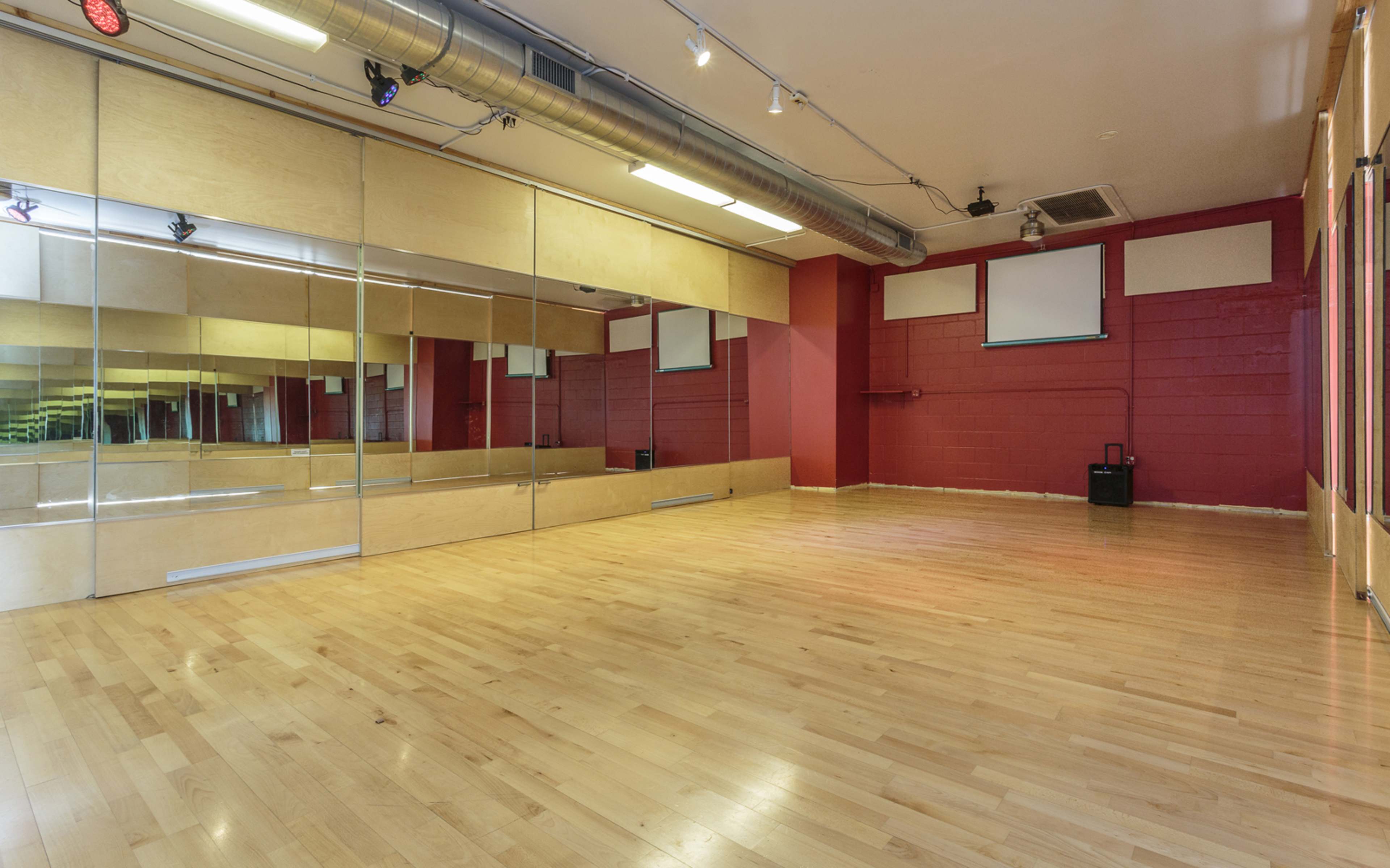 A spacious dance studio with wooden floors, mirrored walls, and red painted accents.