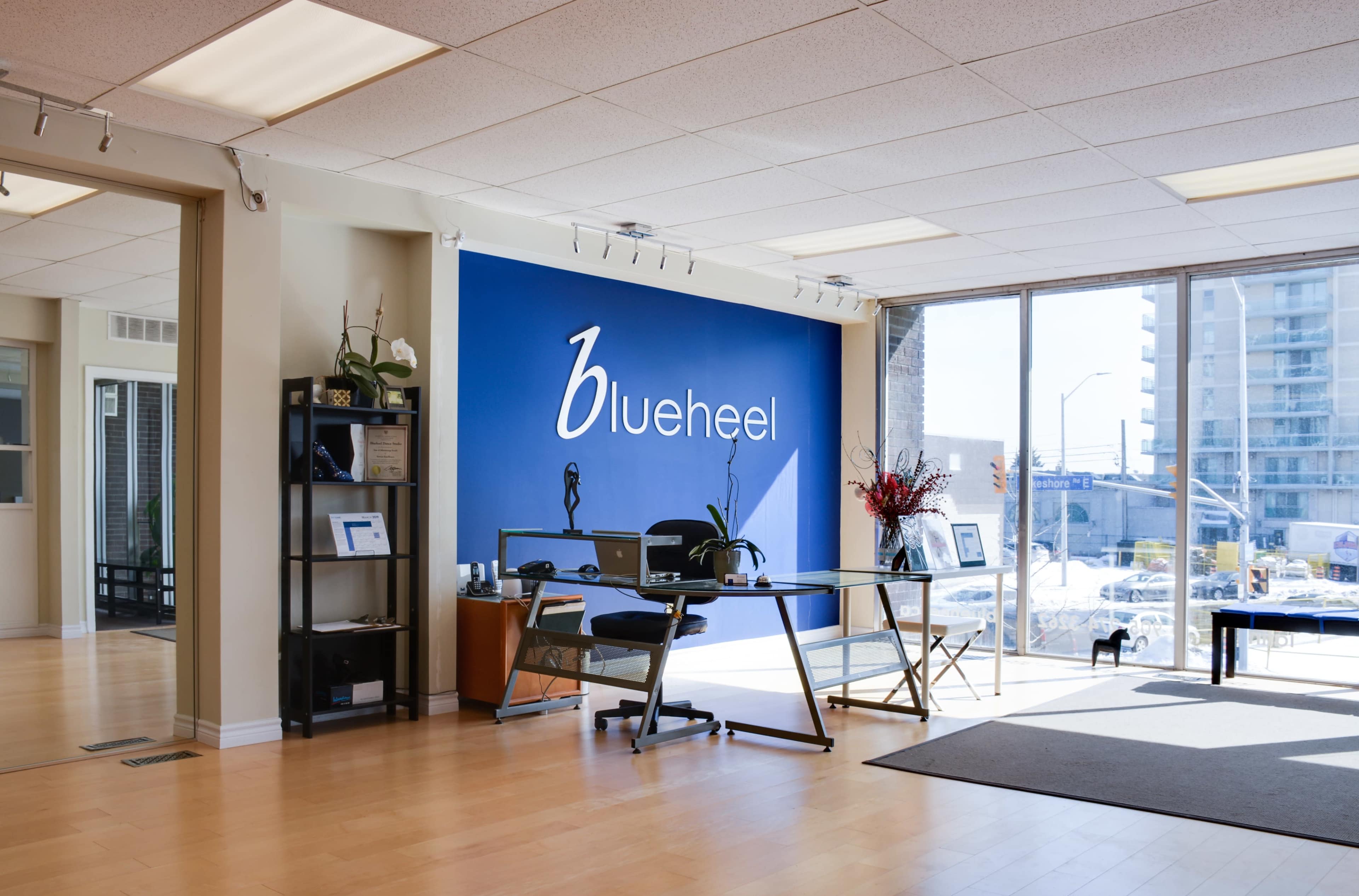 A modern office space with a blue accent wall featuring the logo "blueheel," a glass desk, and a view of the city through large windows.