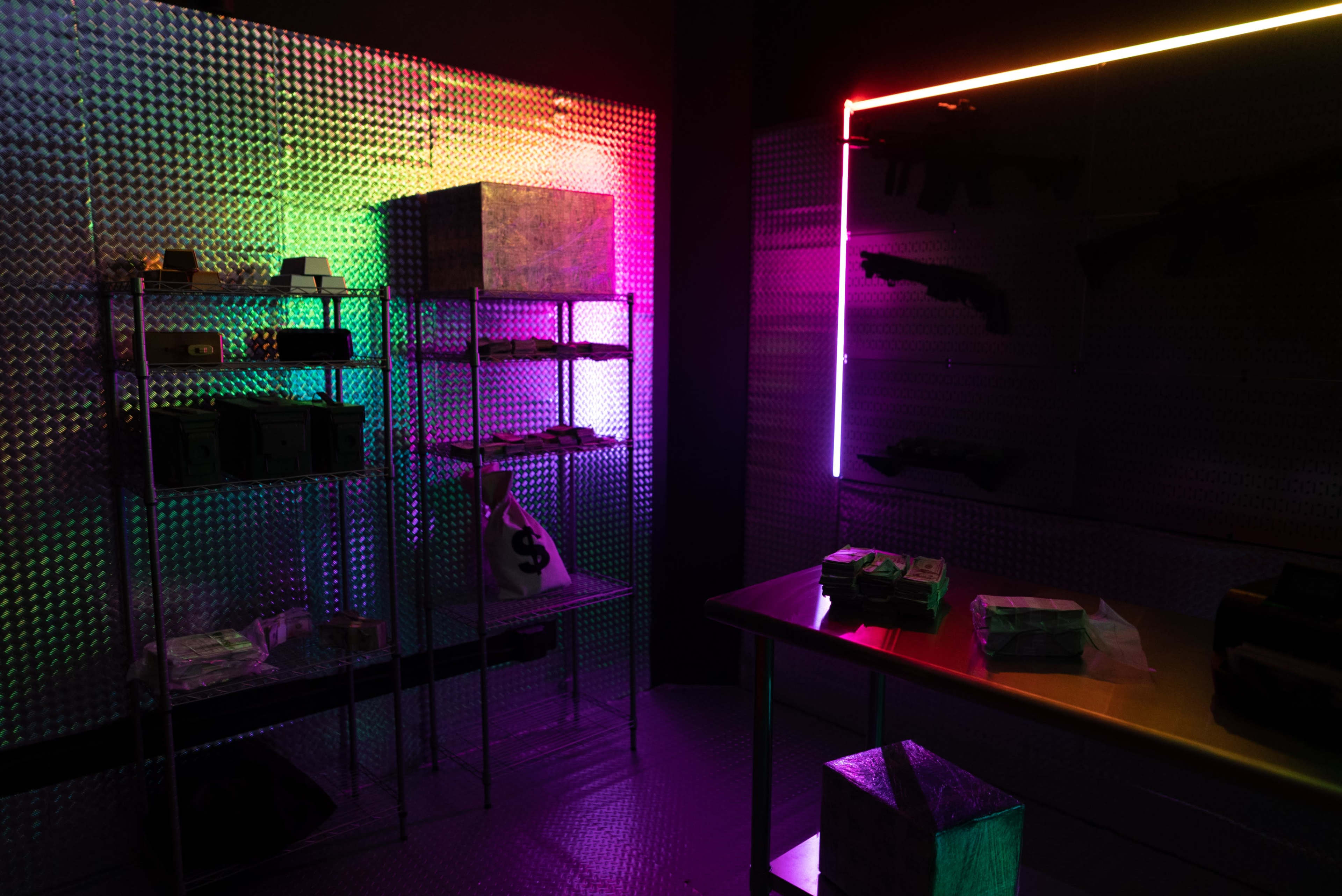The scene features a dimly lit room with colorful neon lights, metal shelves displaying boxes, and stacks of cash on a table.