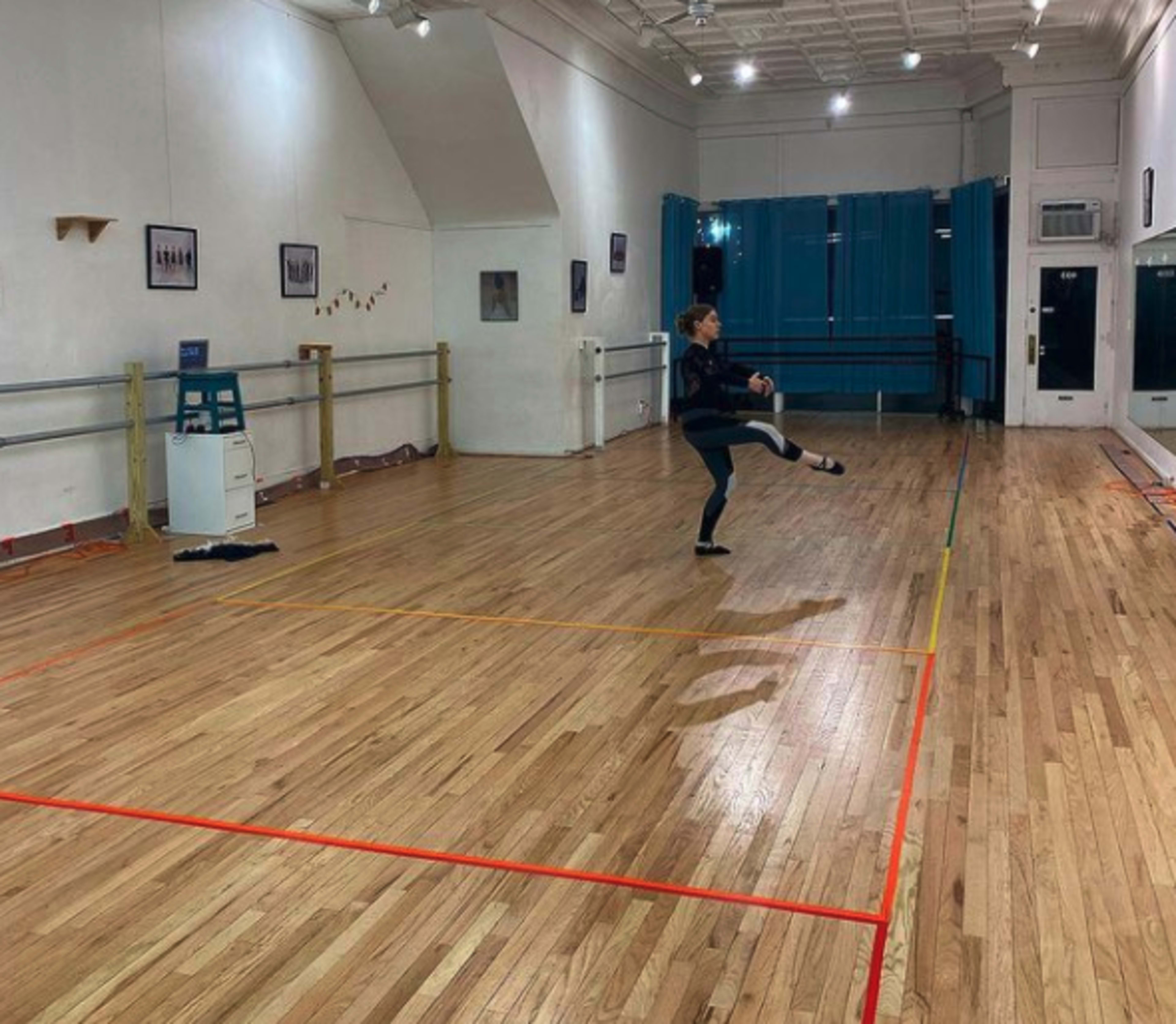 A dancer practices a routine in an empty, well-lit studio with wooden floors and mirrors.