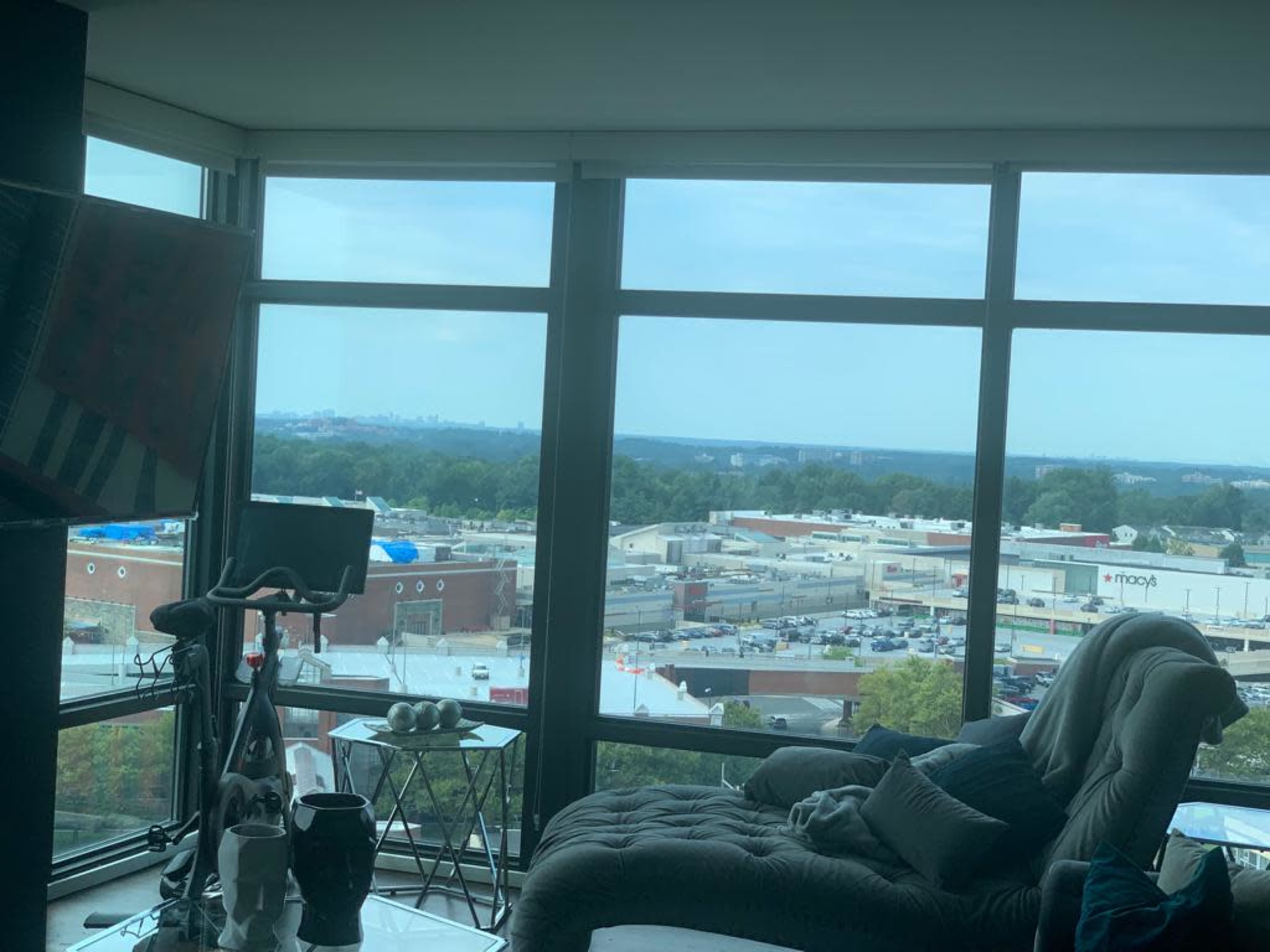 A modern living room features large windows overlooking a shopping center and distant landscape.