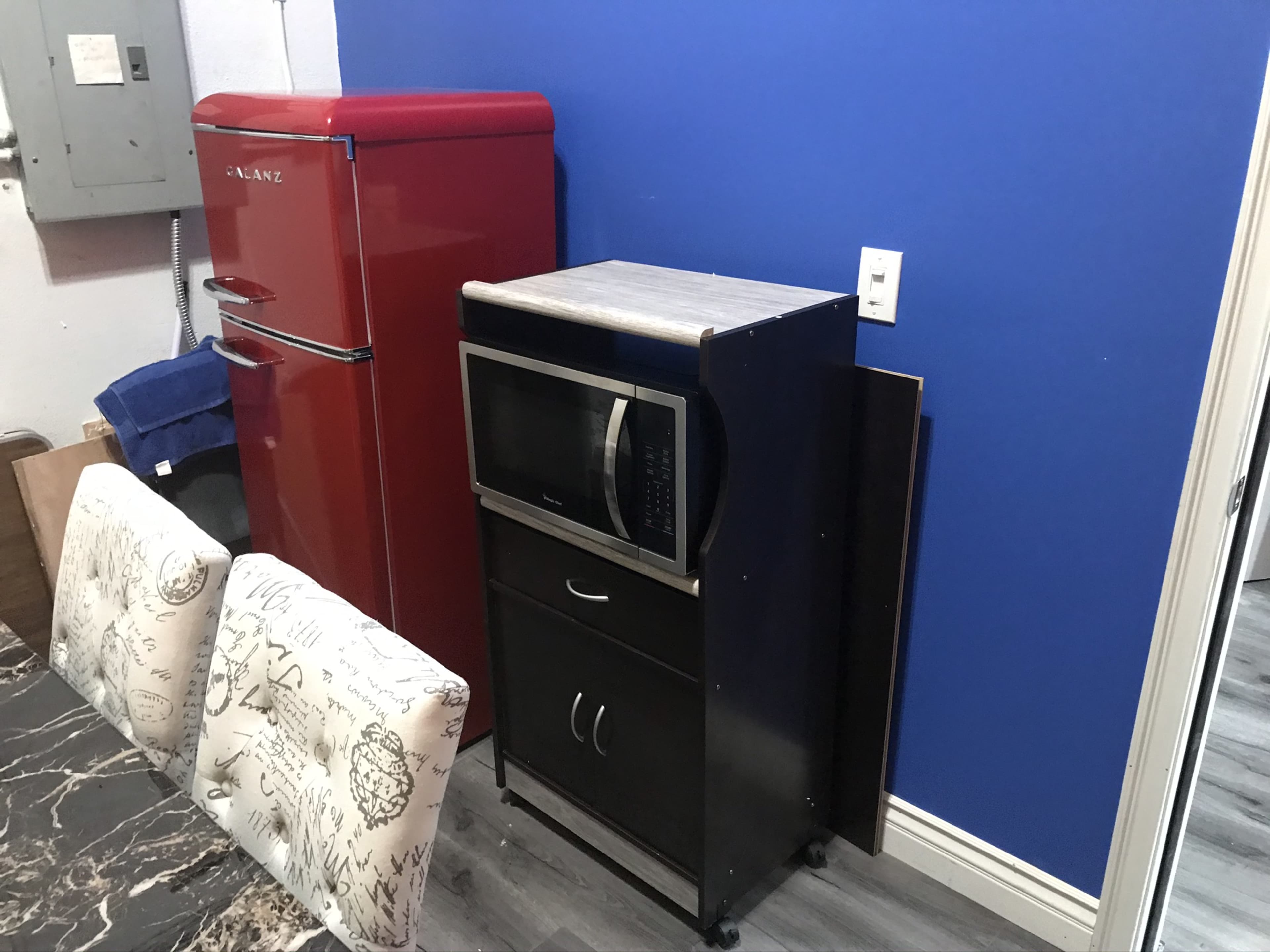 A red refrigerator next to a black microwave cart against a blue wall in a kitchen setting.