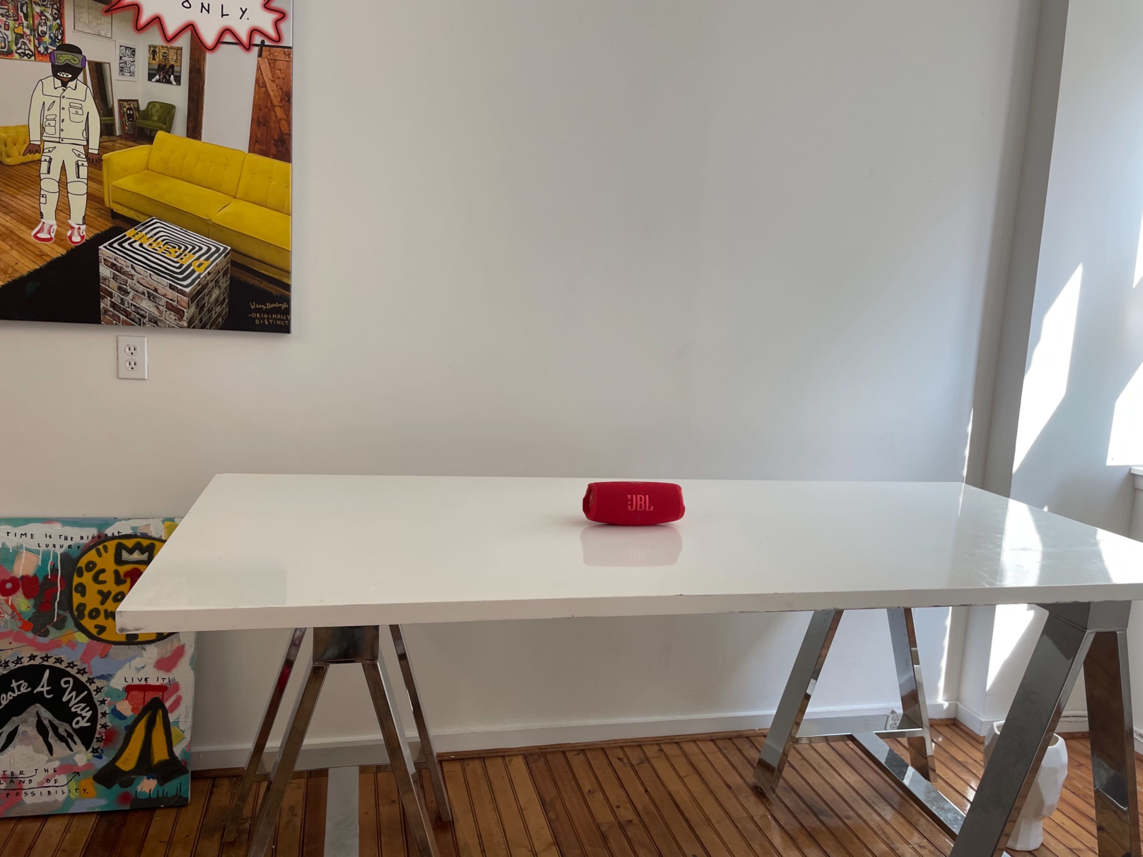A white table sits in a brightly lit room with a red speaker in the center and colorful artwork on the walls.