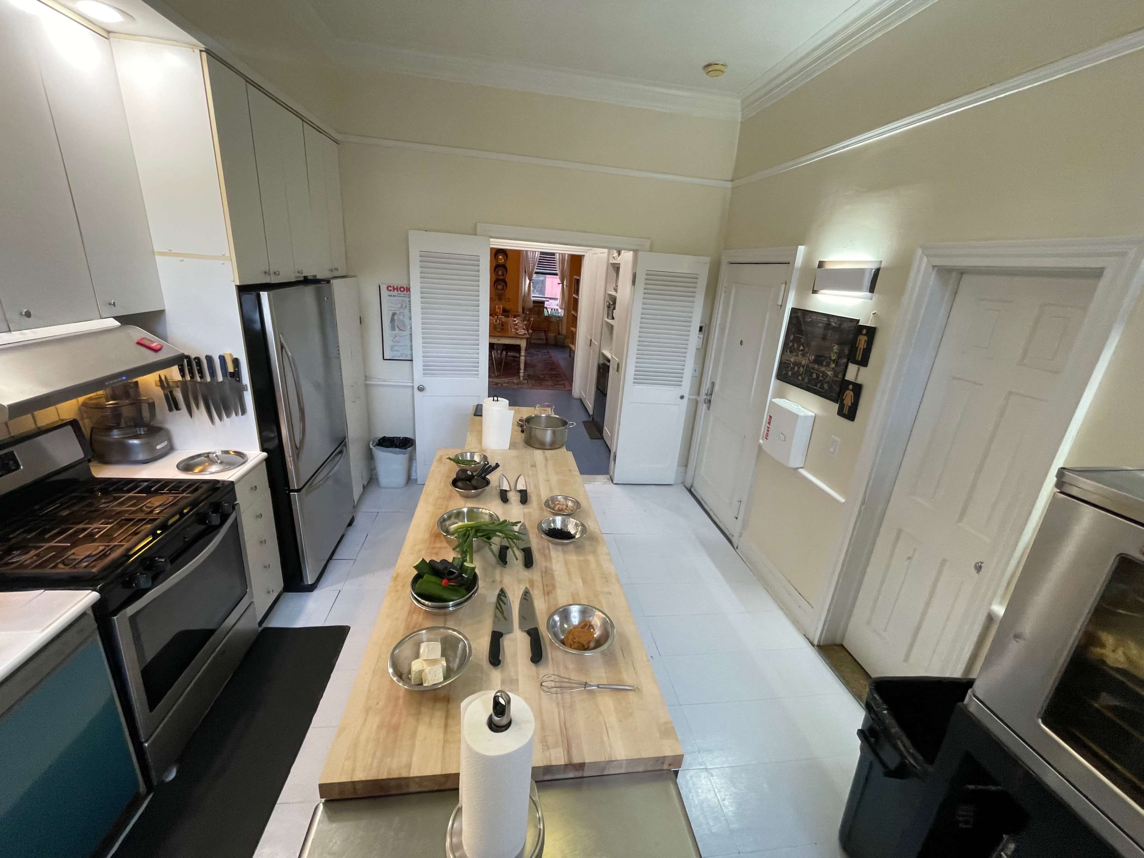 A spacious kitchen features a central wooden prep table with various utensils and ingredients, surrounded by appliances and cabinets.