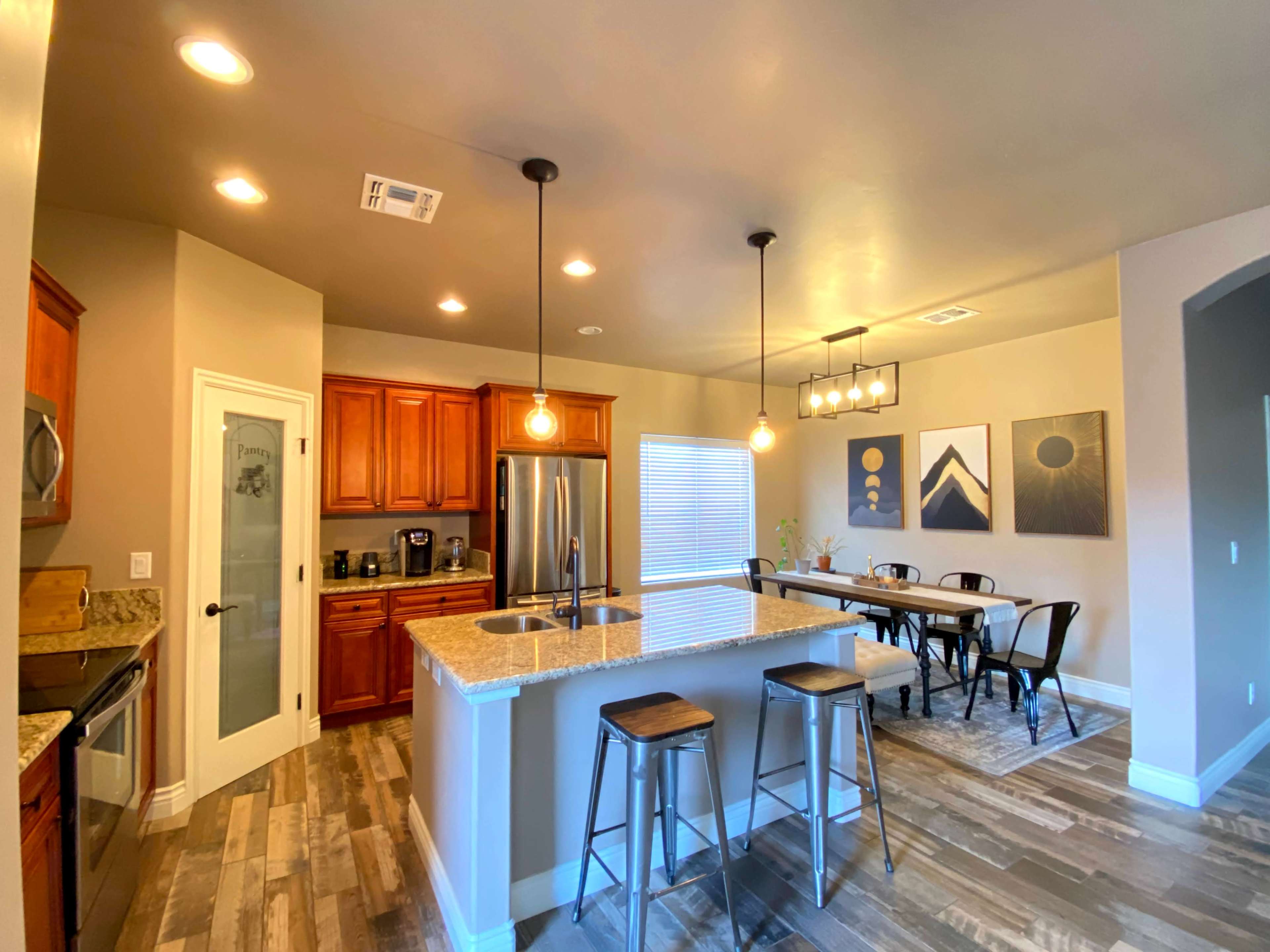 The image shows a modern kitchen with wooden cabinets, granite countertops, and a dining area featuring a table and chairs.