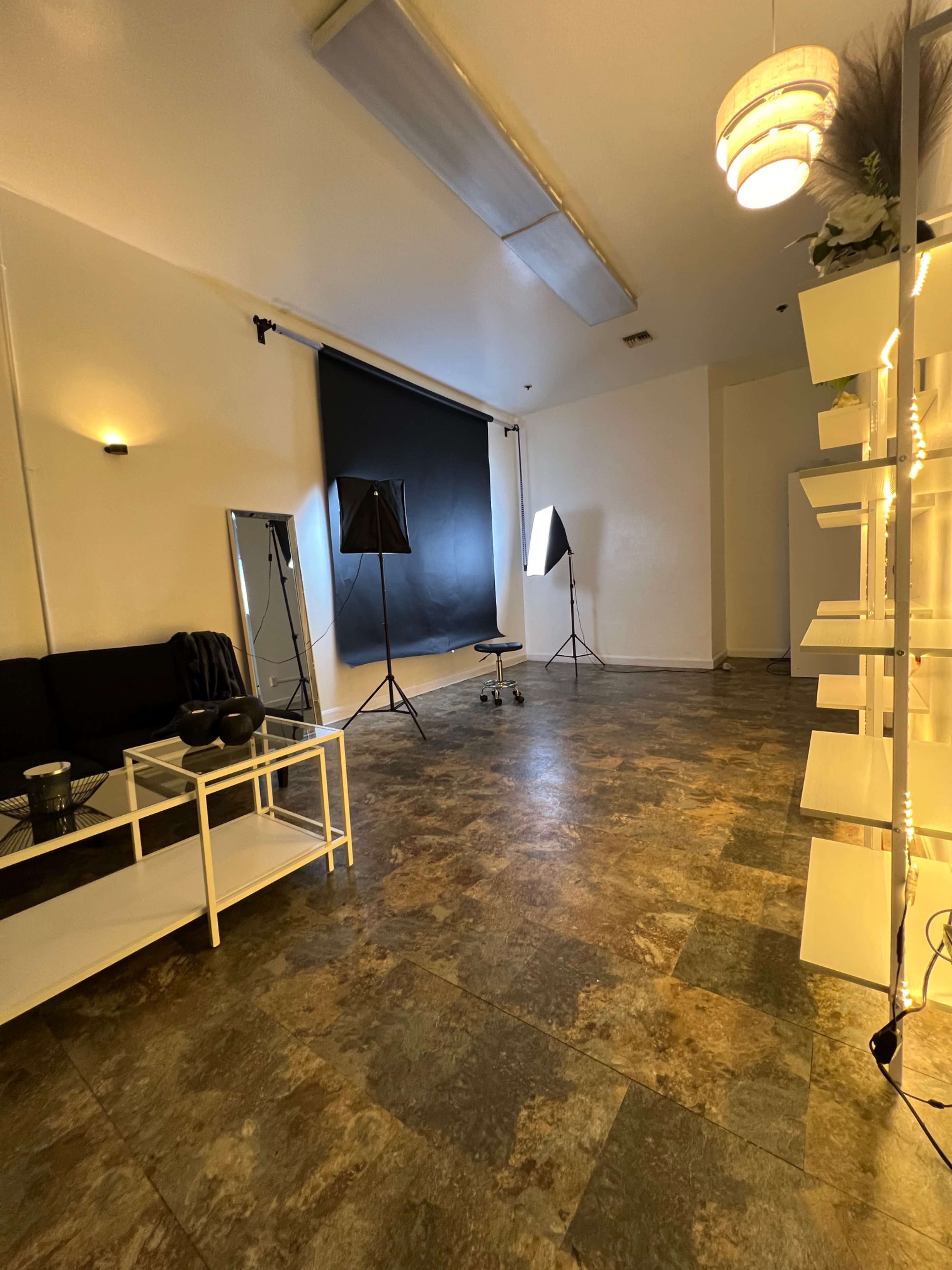 An empty studio space with a black backdrop, two lighting stands, a mirror, and a white shelving unit.