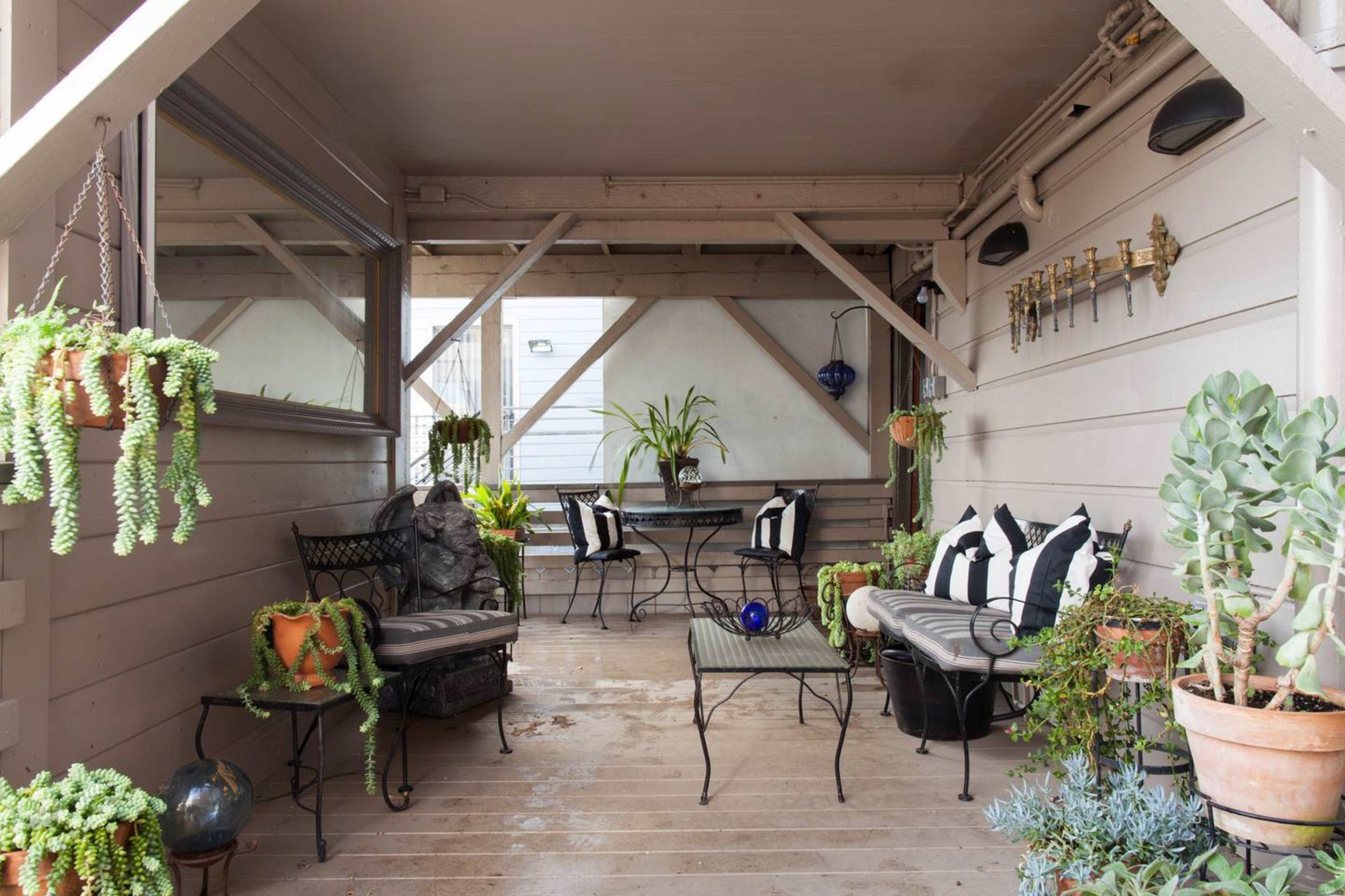 A covered outdoor patio furnished with black and white striped chairs and a table, surrounded by potted plants and hanging greenery.