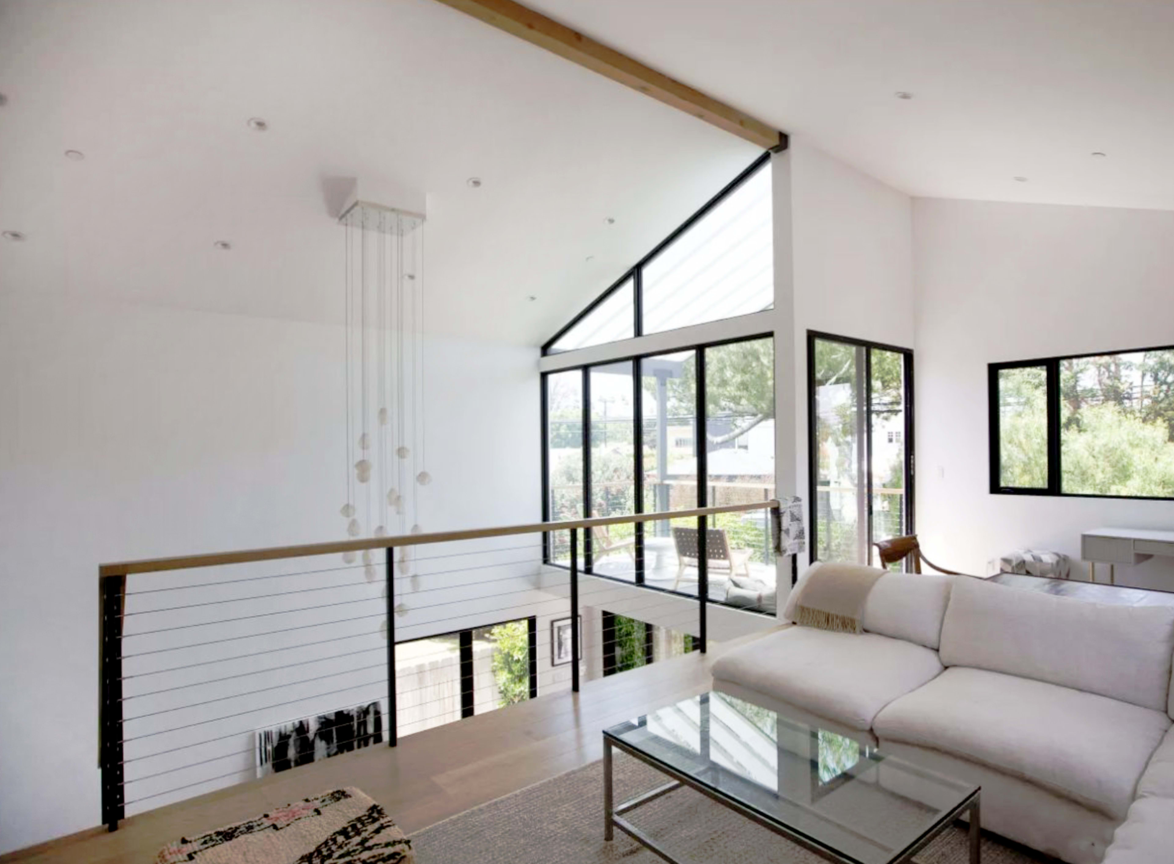 The interior of a modern living room features a white sectional sofa, large windows, and a minimalist design with wooden flooring.