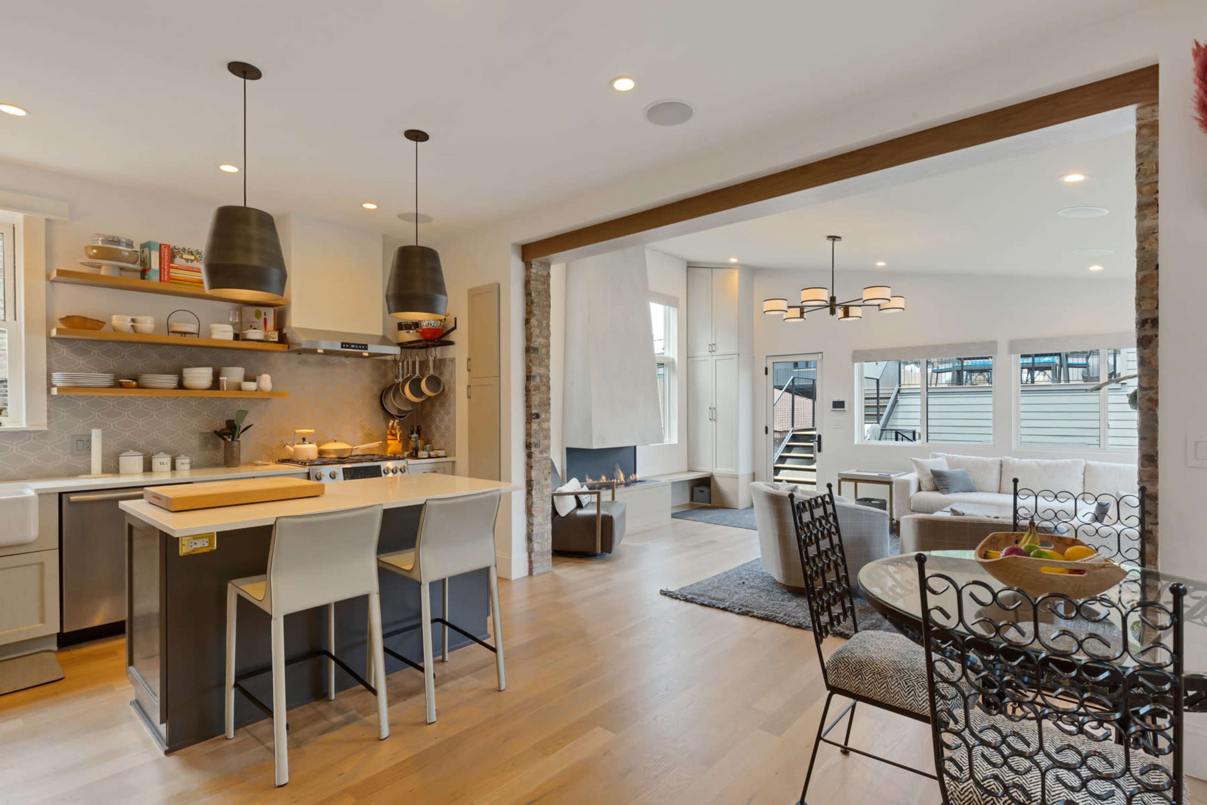 The image shows a modern kitchen with a breakfast bar, open to a living area featuring a circular dining table and a seating arrangement.