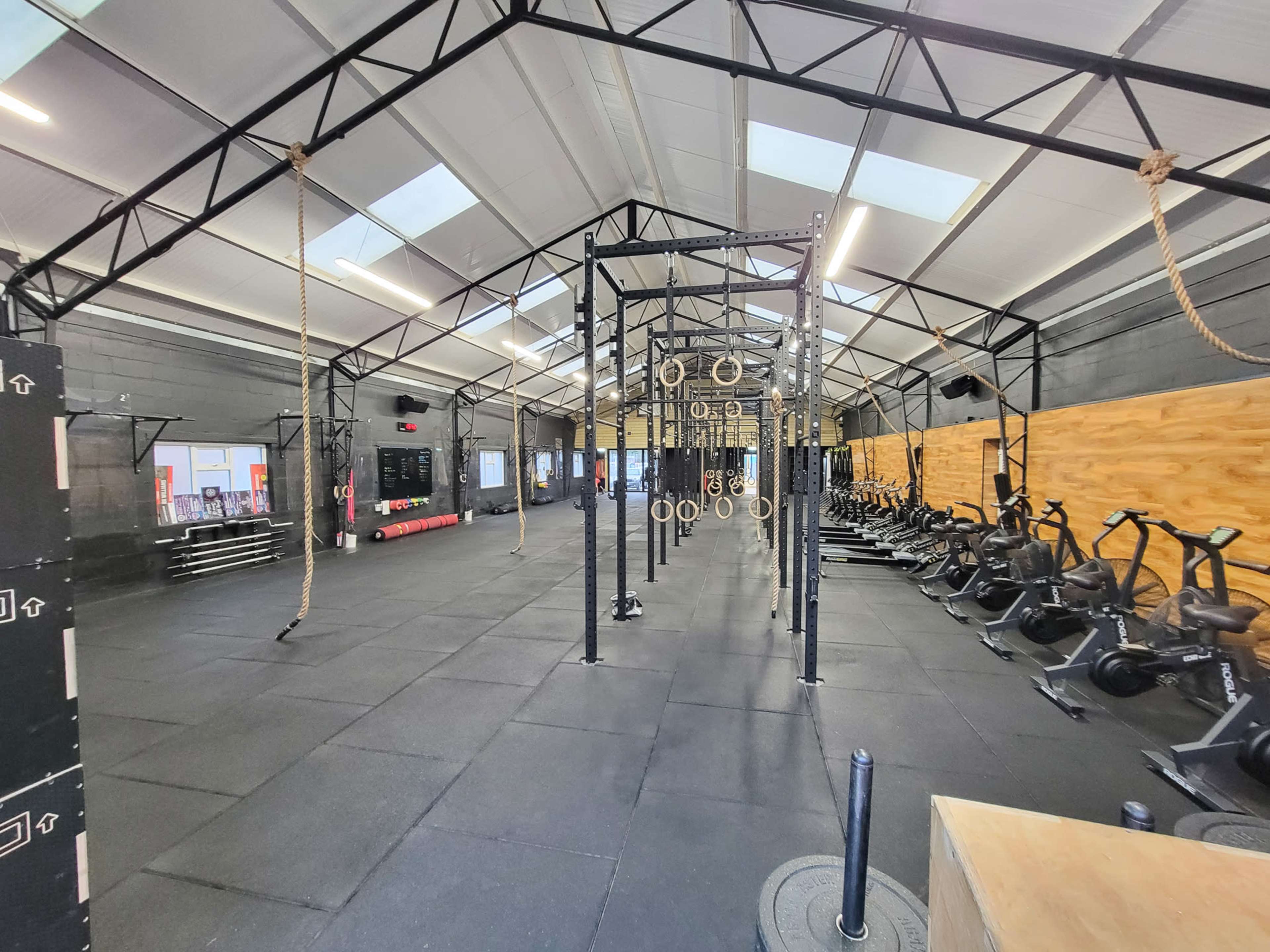 The image shows an empty gym with various exercise equipment arranged in the space, including rowing machines and a section for cross-training activities.