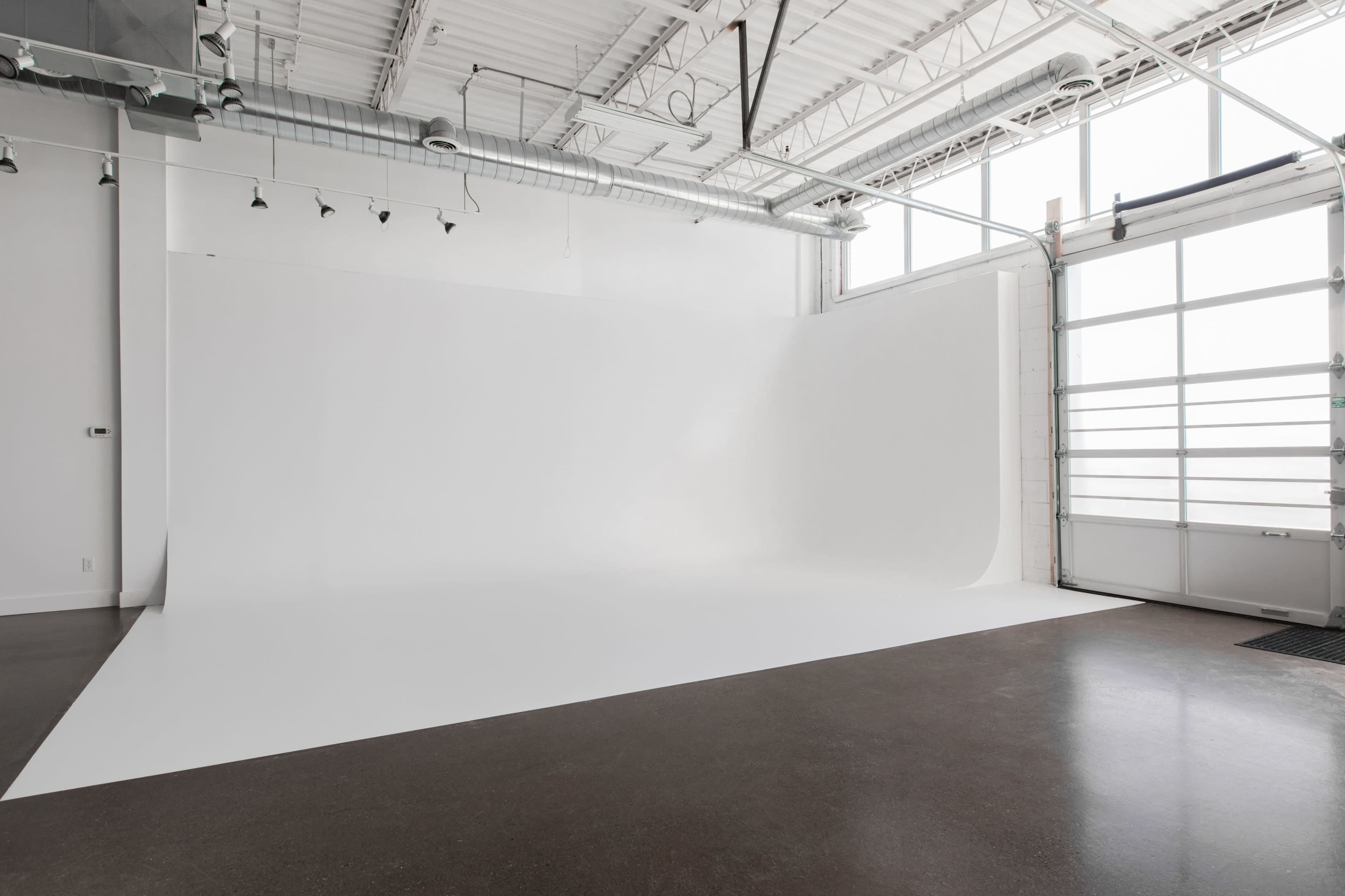 A spacious, empty studio with a seamless white backdrop and large windows letting in natural light.