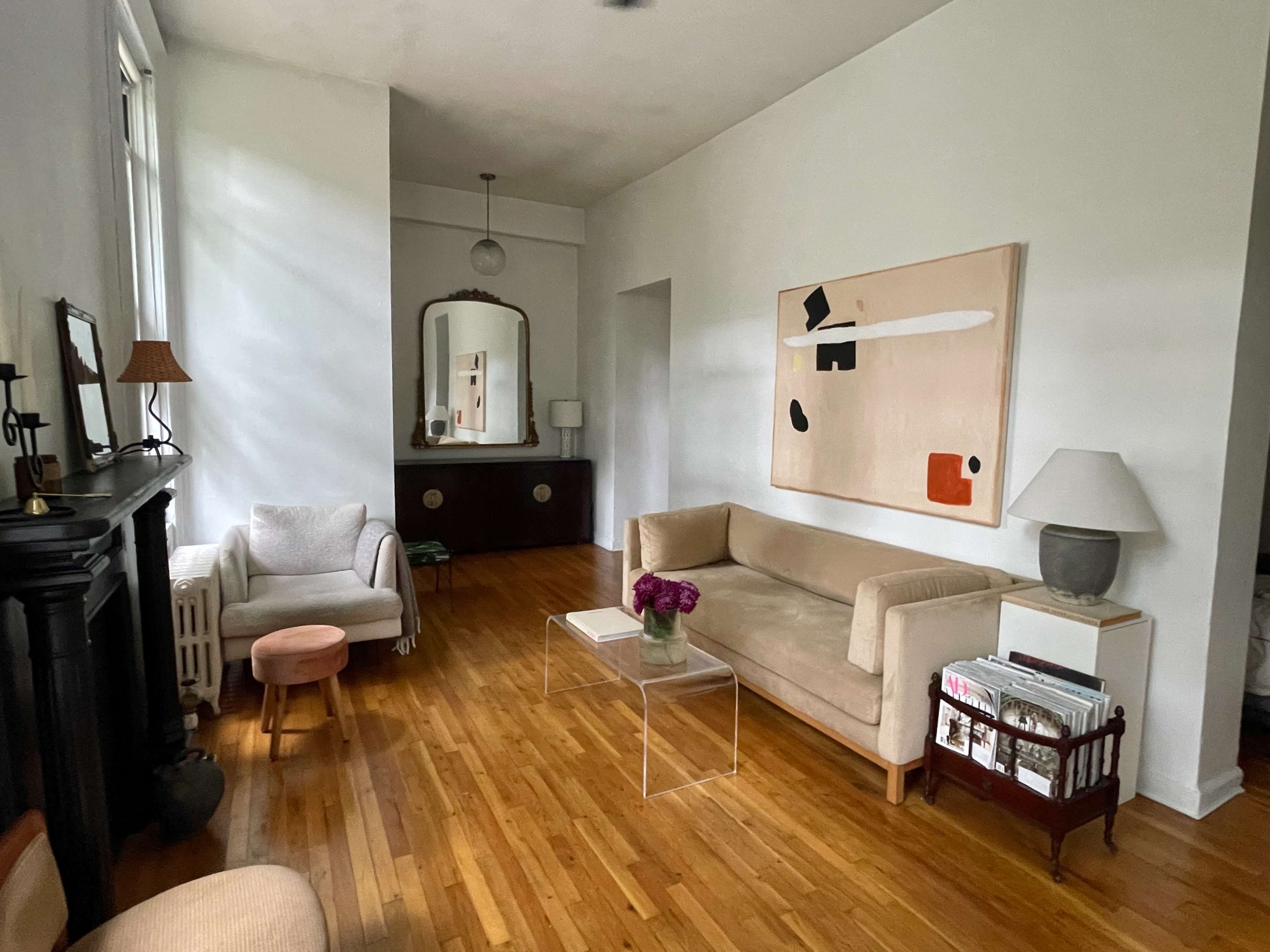 A living room with wooden flooring, a beige couch, a clear coffee table, a lamp, and a large abstract painting on the wall.