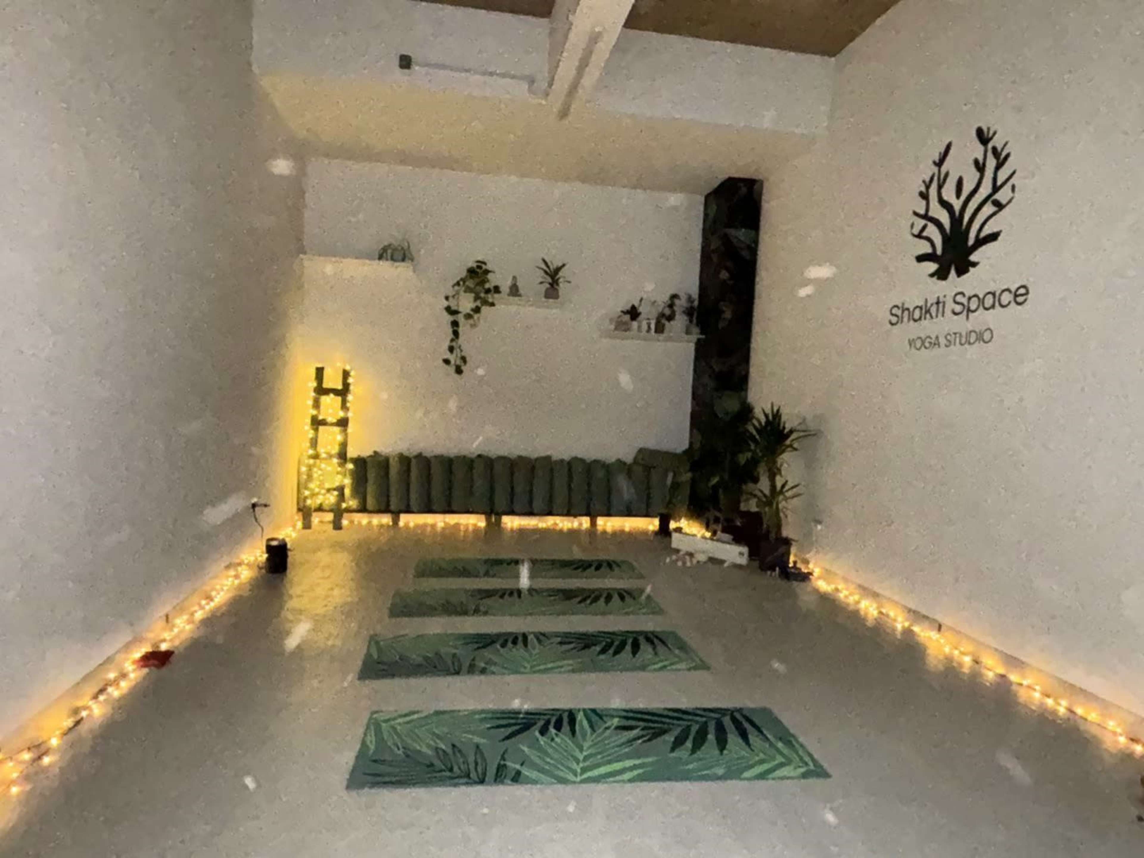 The image shows a yoga studio with three green mats arranged on the floor, surrounded by soft lighting and decorative plants.