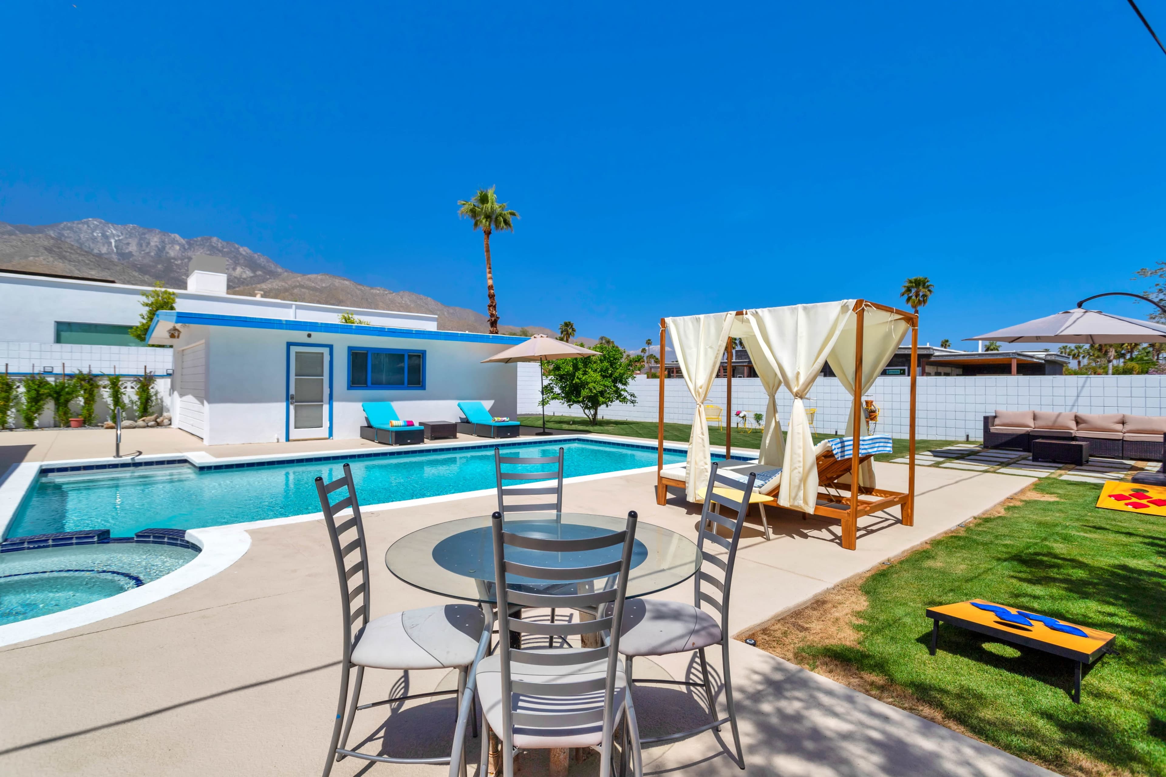 The scene features a modern backyard with a swimming pool, lounge chairs, a shaded cabana, and a grassy area with outdoor seating in a sunny environment.