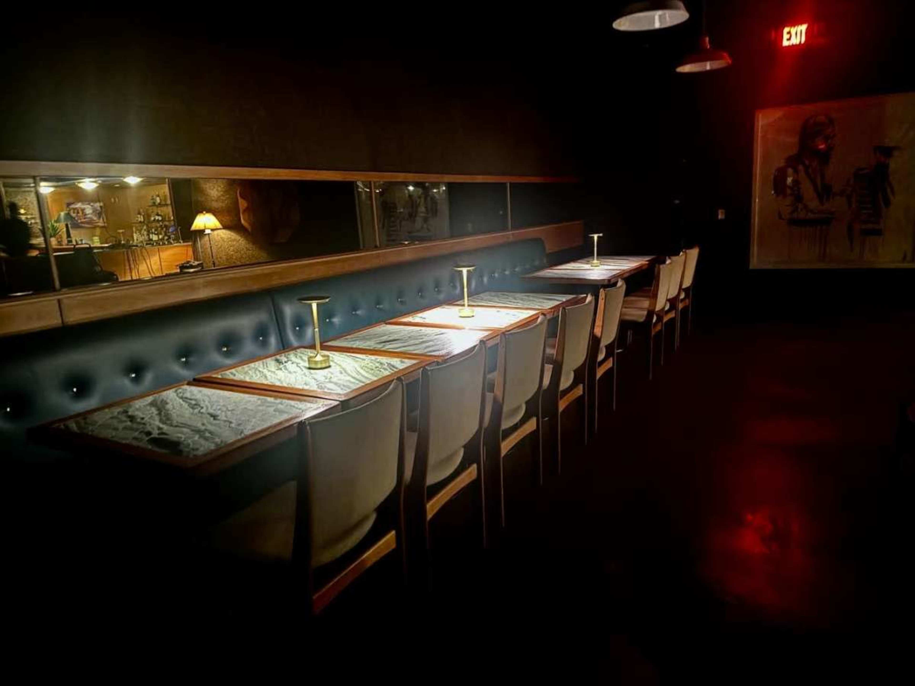 A dimly lit restaurant features a row of tables with marble tops and brass lamps against a dark backdrop.
