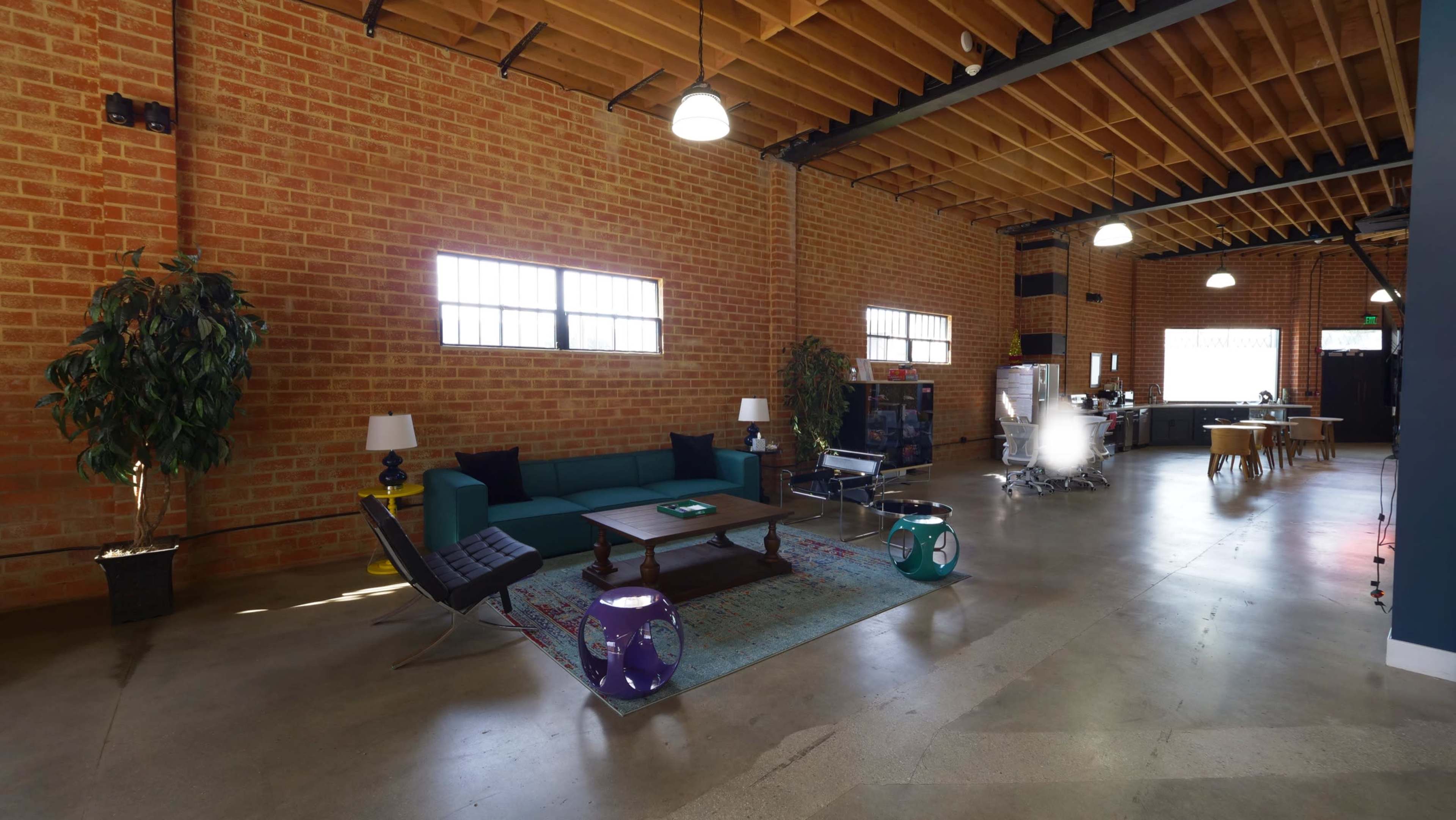A spacious room features brick walls, a green couch, a coffee table, and a kitchen area in the background.
