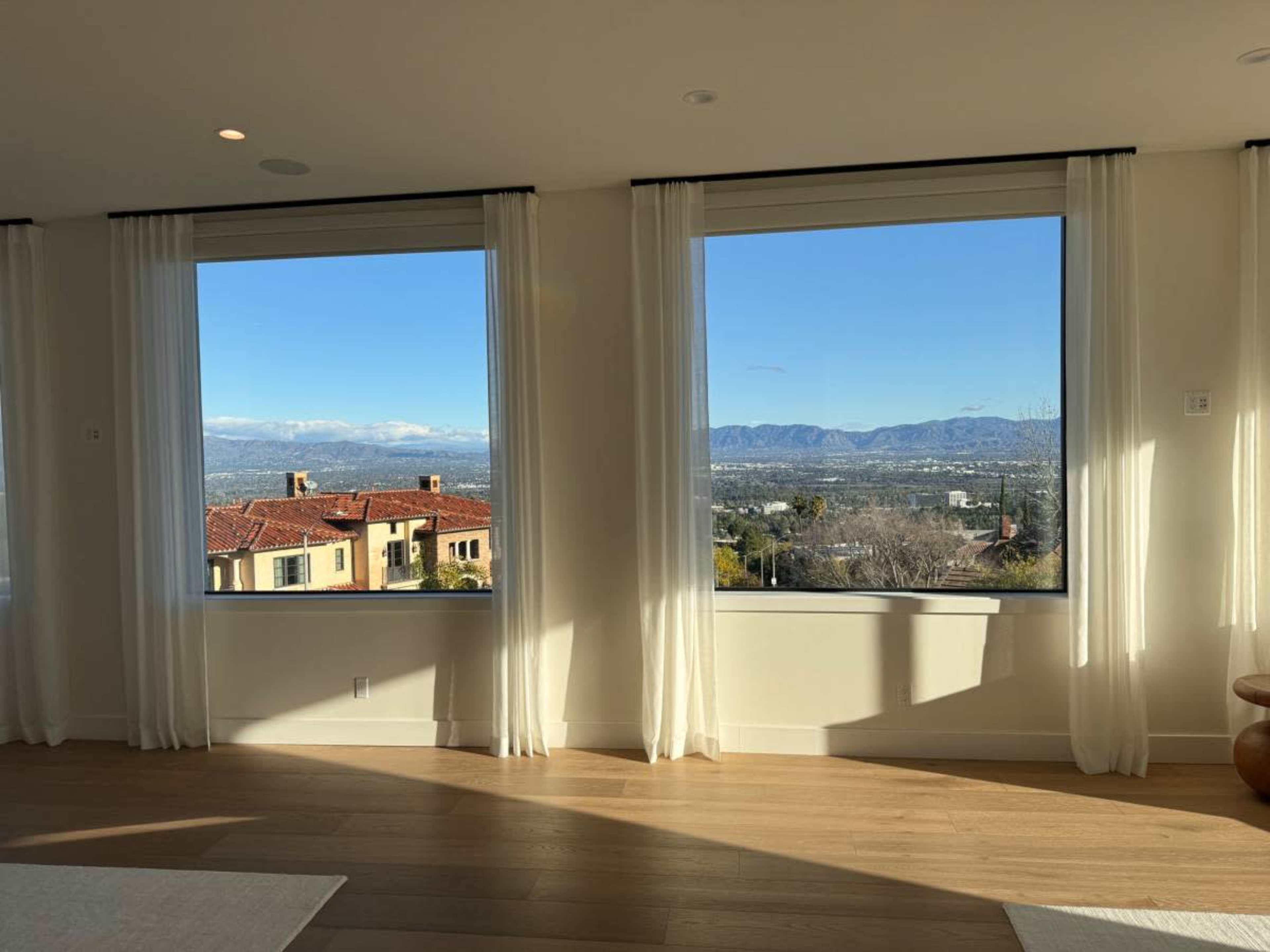 The image shows a modern interior with large windows revealing a view of mountains and a landscape below.